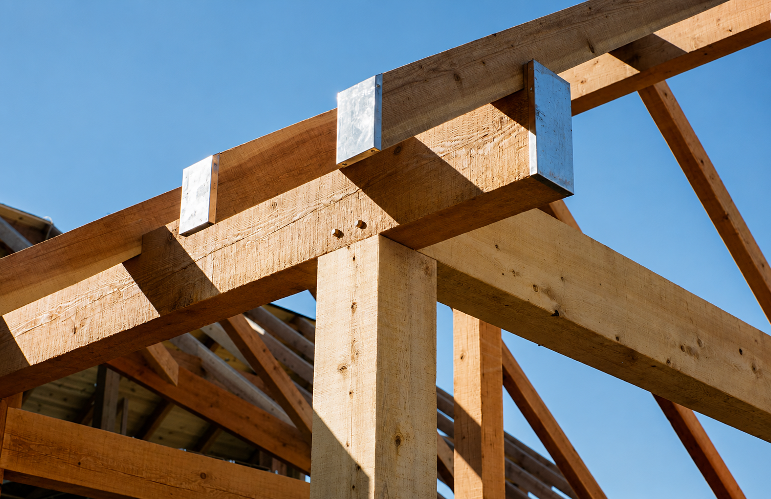 Close-up of wooden construction beams and metal connectors at a building site under a clear blue sky.