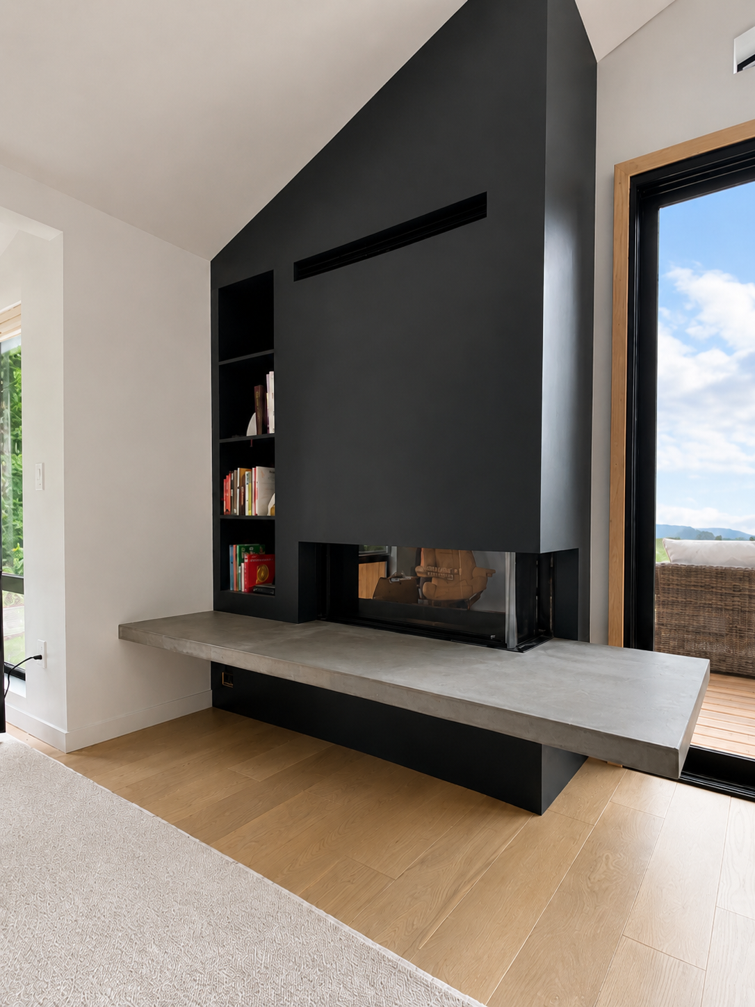 Modern living room with black fireplace and built-in bookshelf on black wall, large window showing outdoor scenery, beige carpet, and light wood flooring.