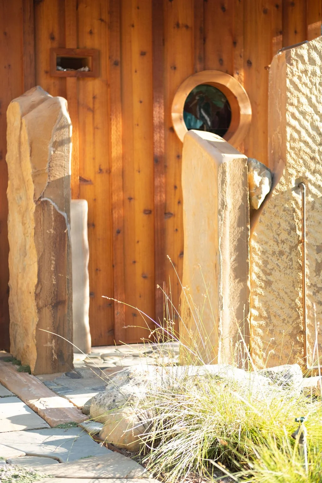 Wooden wall with a circular window, stone sculptures, and desert plants in the foreground.