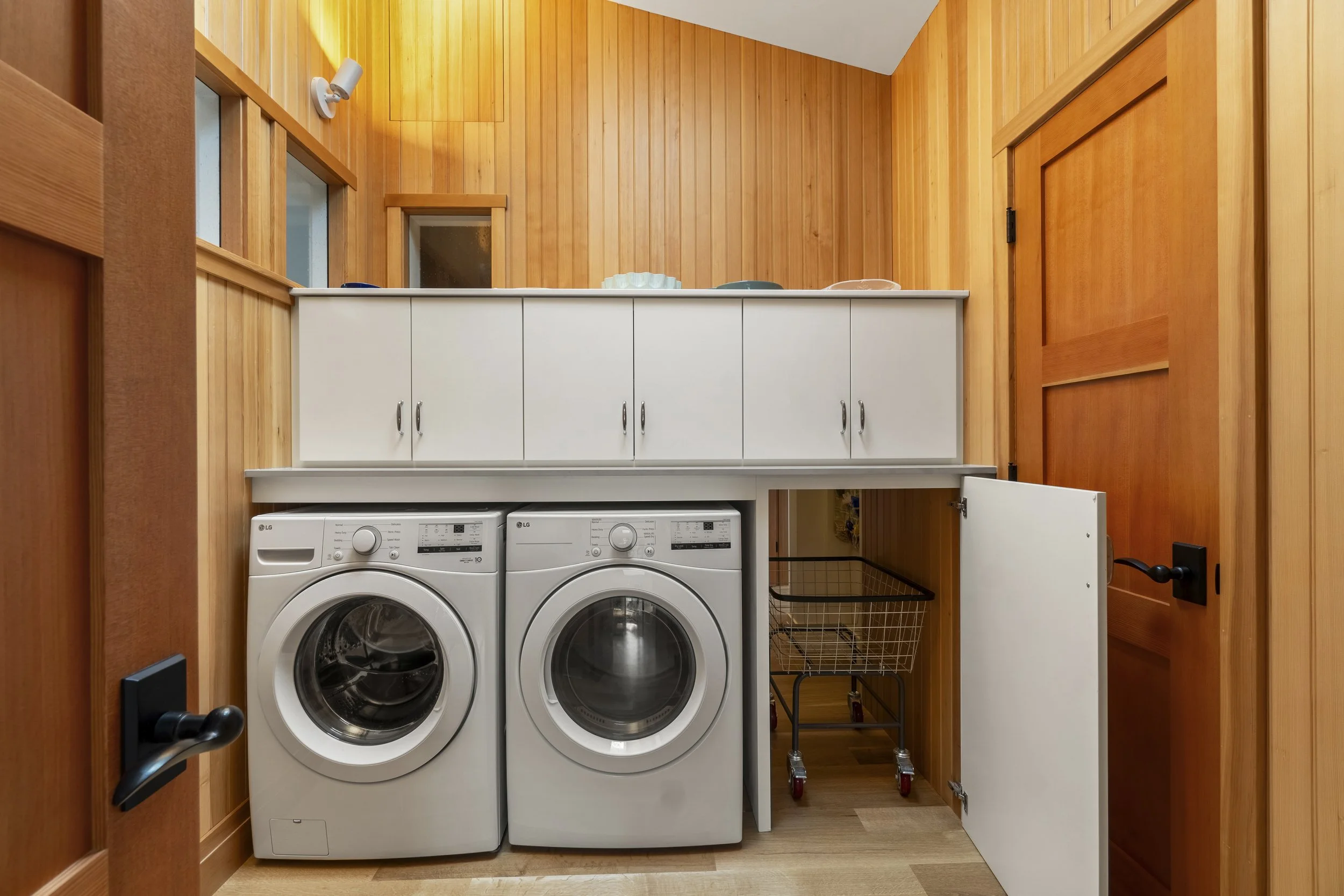 A laundry room with wood-paneled walls, a white cabinet, a washing machine, and a dryer.