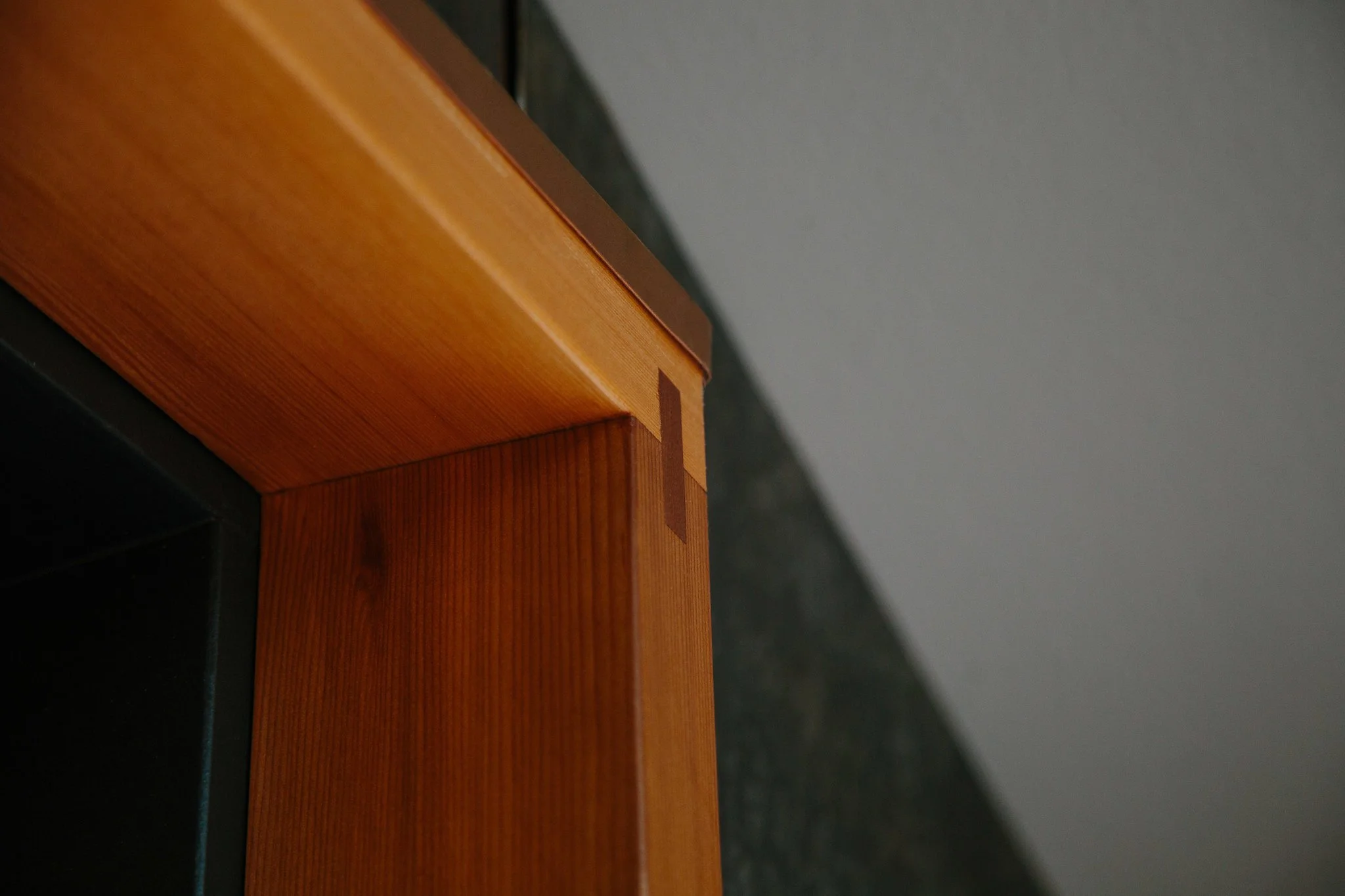 Close-up of the corner of a wooden piece of furniture with a smooth, varnished surface, against a gray wall.