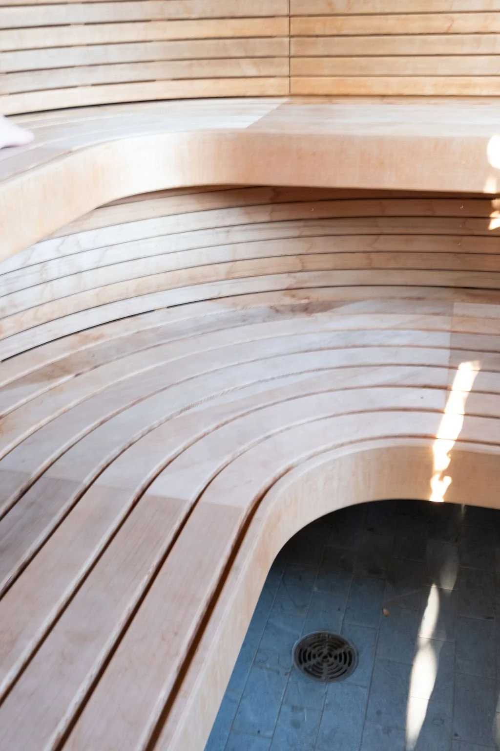 Curved wooden benches with a drain on the floor and wooden wall in the background.