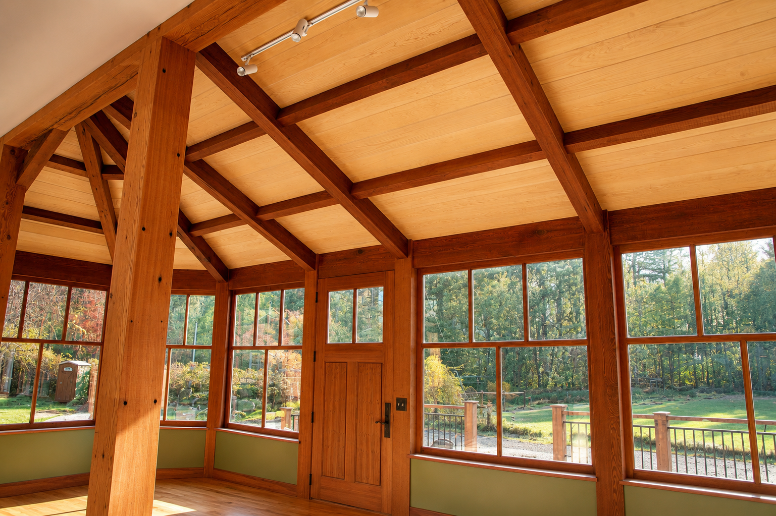 Interior of a sunroom with wooden beams and large windows overlooking a garden with trees and a lawn.