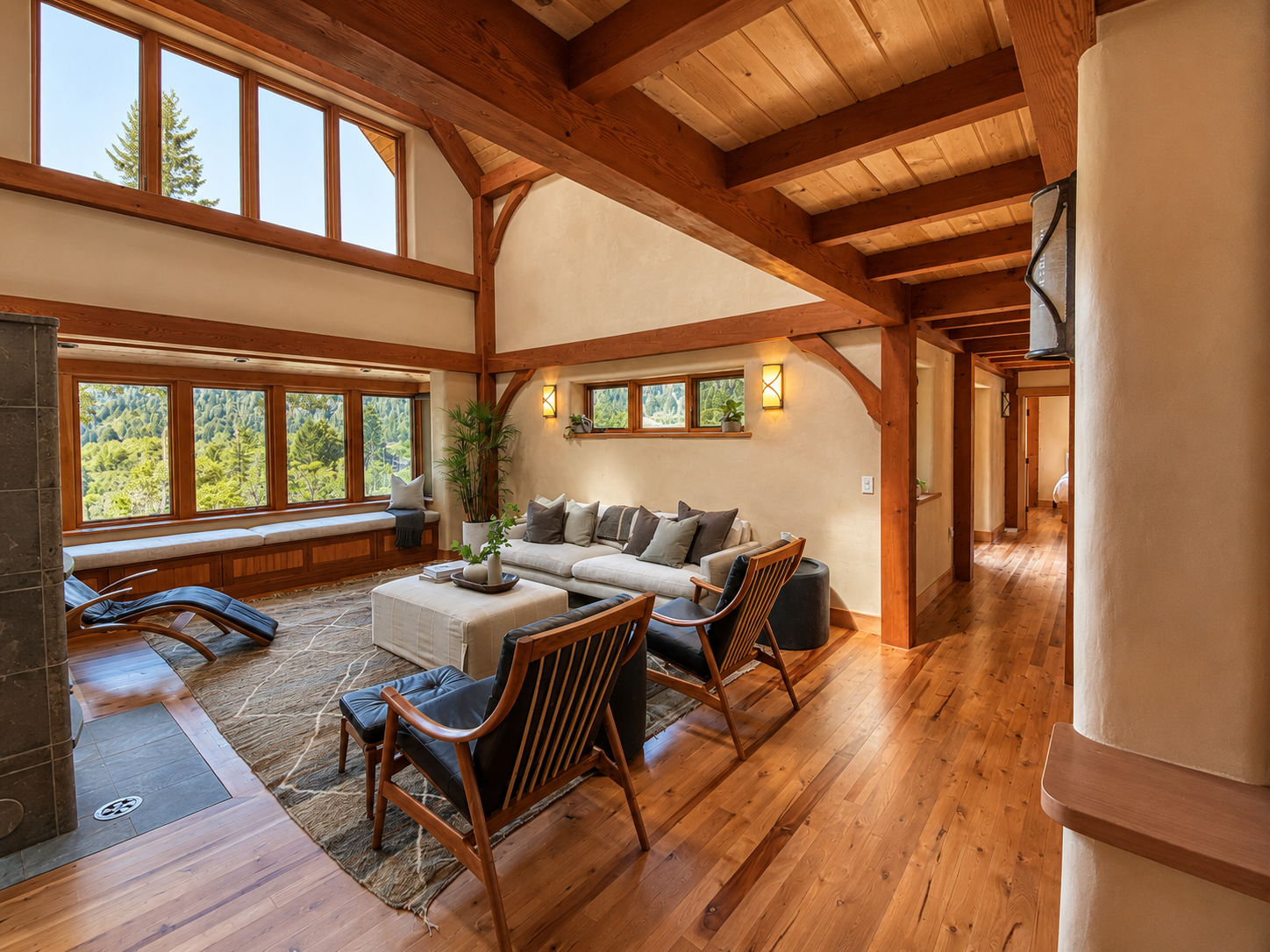 Living room with large windows, wooden beams, beige walls, white sofa, black lounge chair, wooden floor, plants, and hallway.