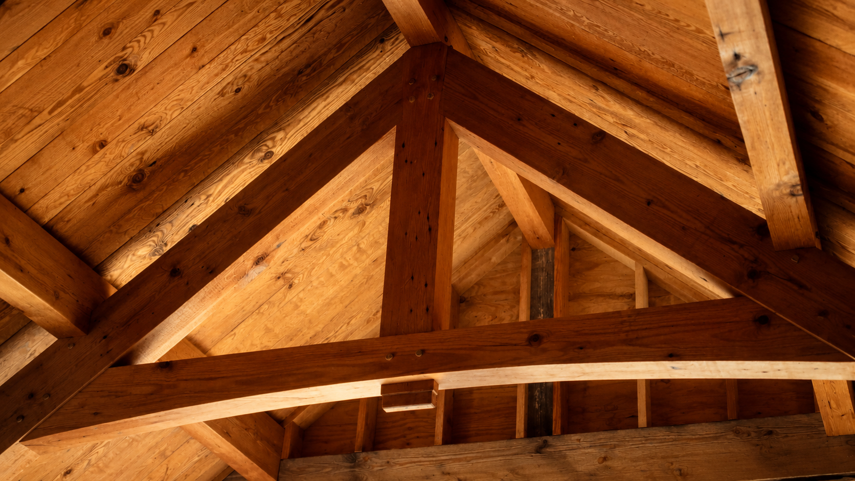 Interior view of a wooden roof structure with beams and plywood panels.