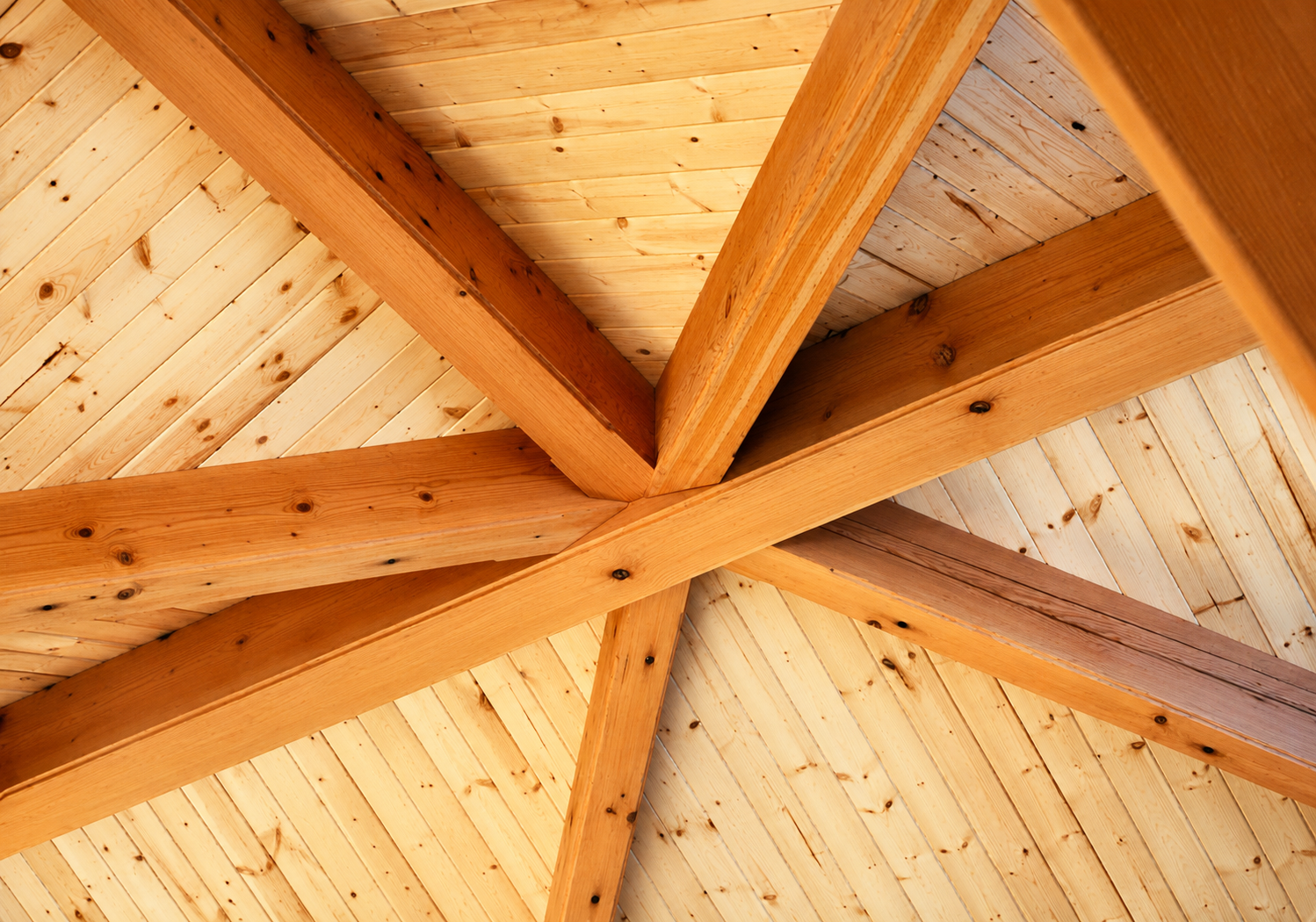 Close-up view of a wooden ceiling with intersecting beams and plywood panels.