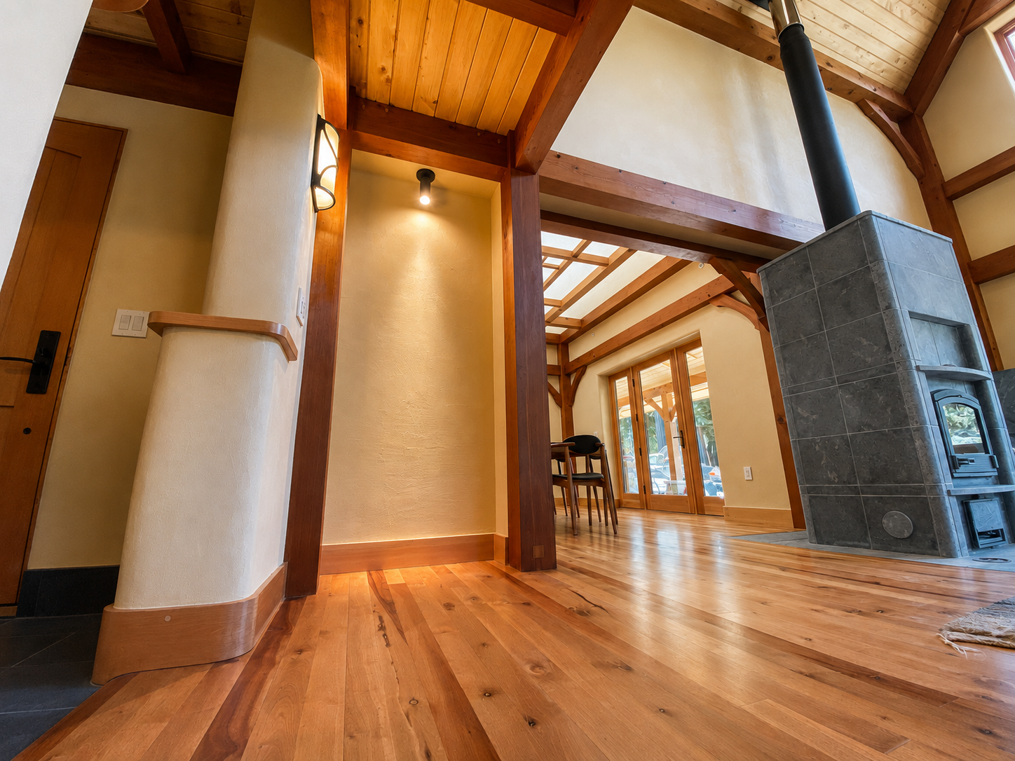 Interior view of a room with wooden beams, hardwood flooring, a gray tile fireplace, and large glass doors leading to an outdoor area.