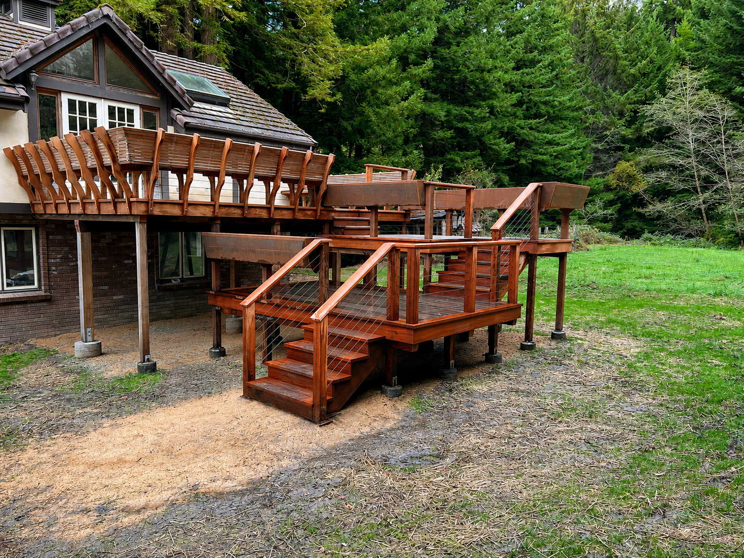 A wooden deck attached to a house, with a staircase leading down to the yard, surrounded by trees and greenery.