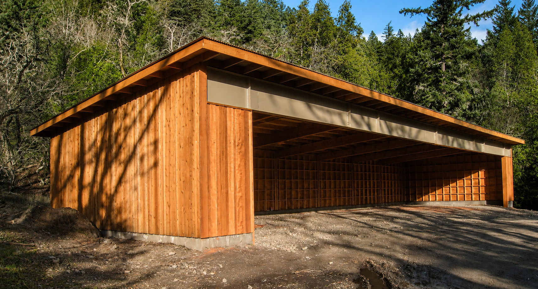 A wooden garage or storage shed with a sloped roof, situated outdoors in a natural setting with trees and greenery in the background.