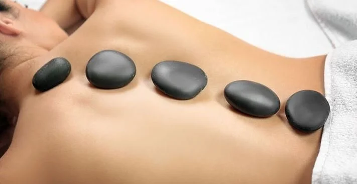 A person receiving hot stone massage with six smooth black stones placed along their back.