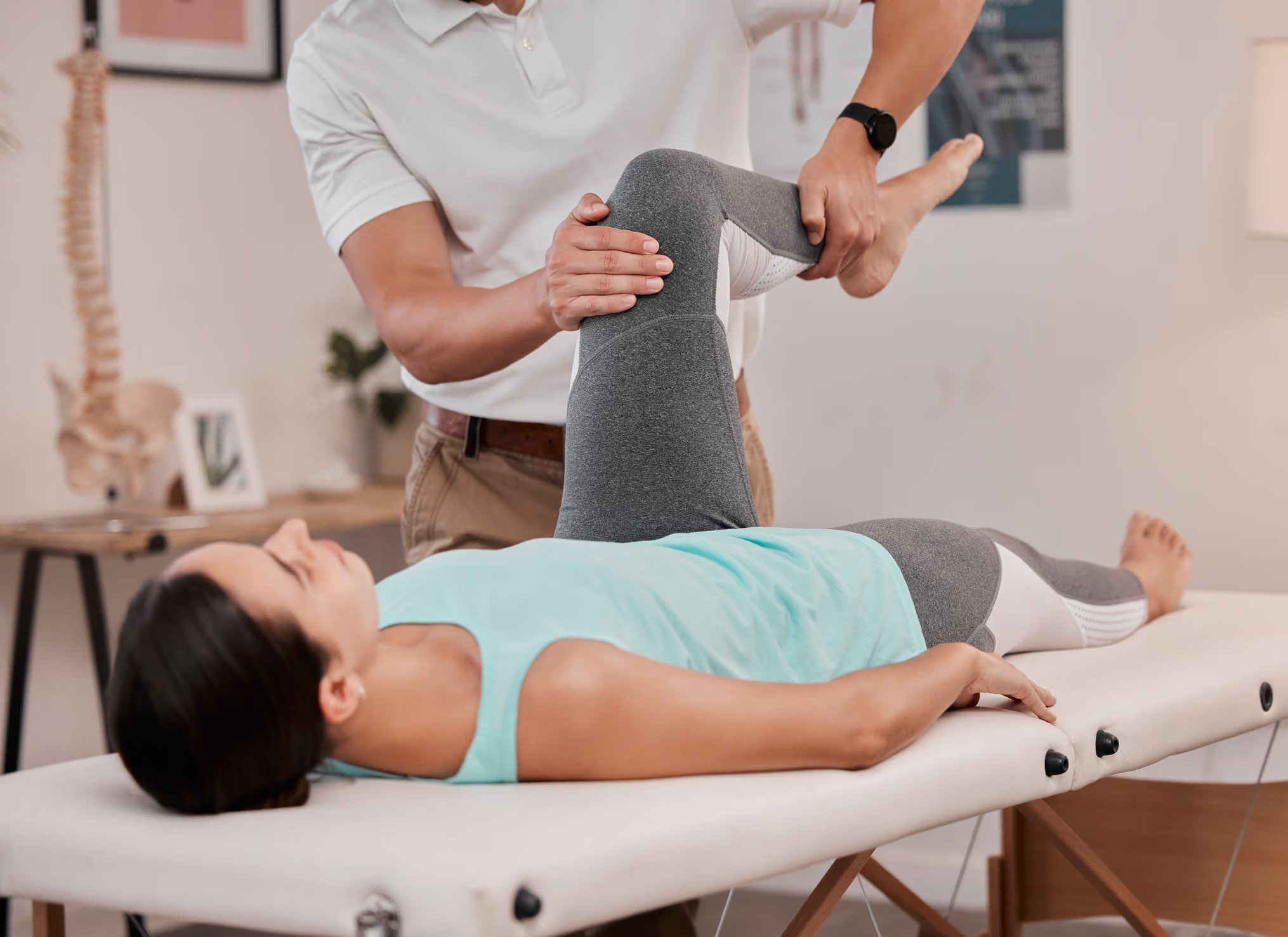 Physical therapy session with a woman lying on a treatment table, receiving knee therapy from a therapist in a clinical setting.