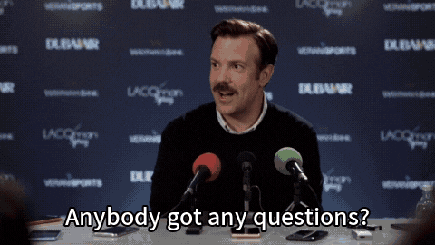 a gif of Ted from Ted Lasso asking if anyone has questions at a press conference after a game. Everyone in the crowd raises their hand with a question.