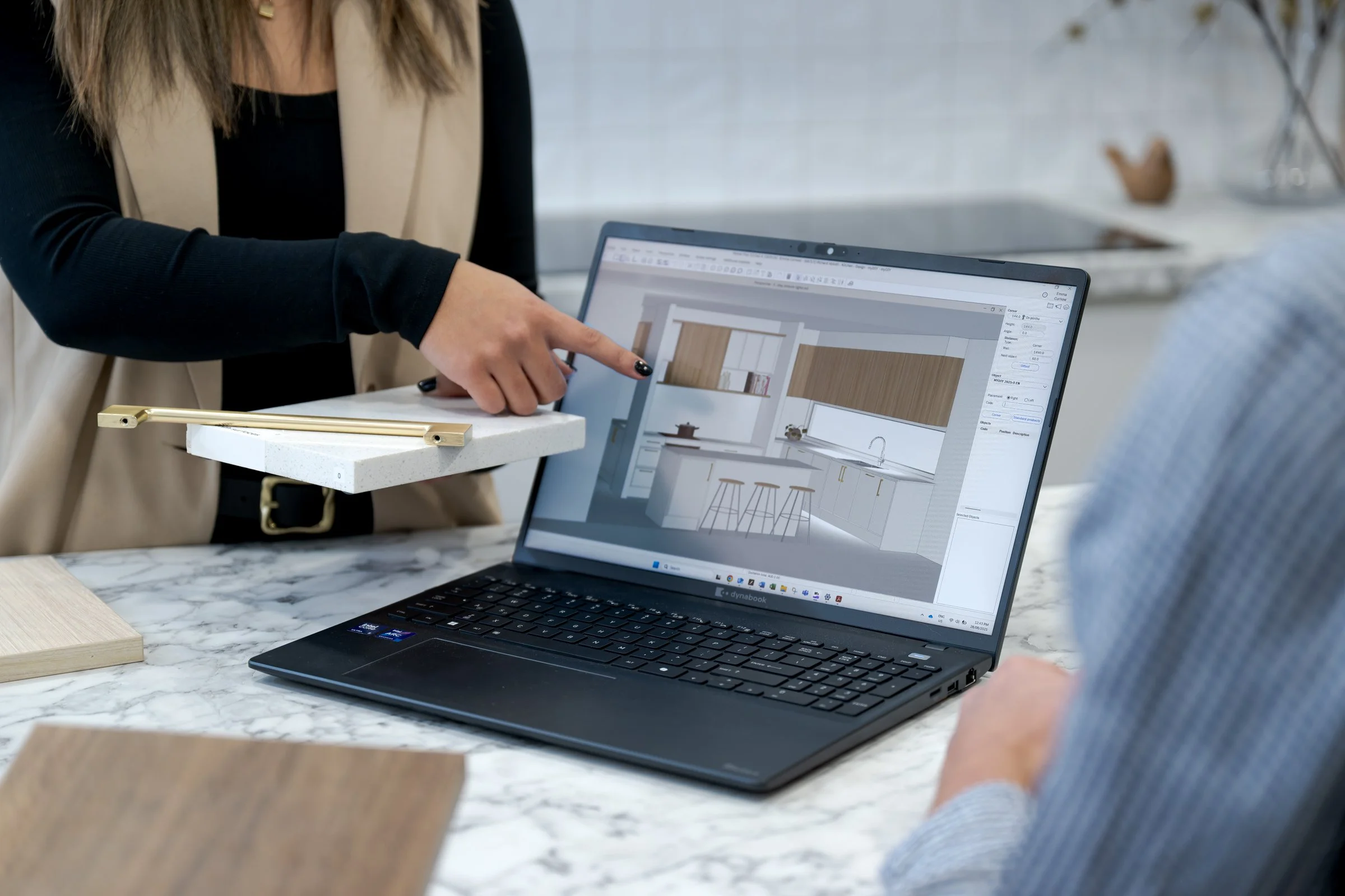 Person pointing at a laptop screen showing a kitchen interior design plan during a meeting.