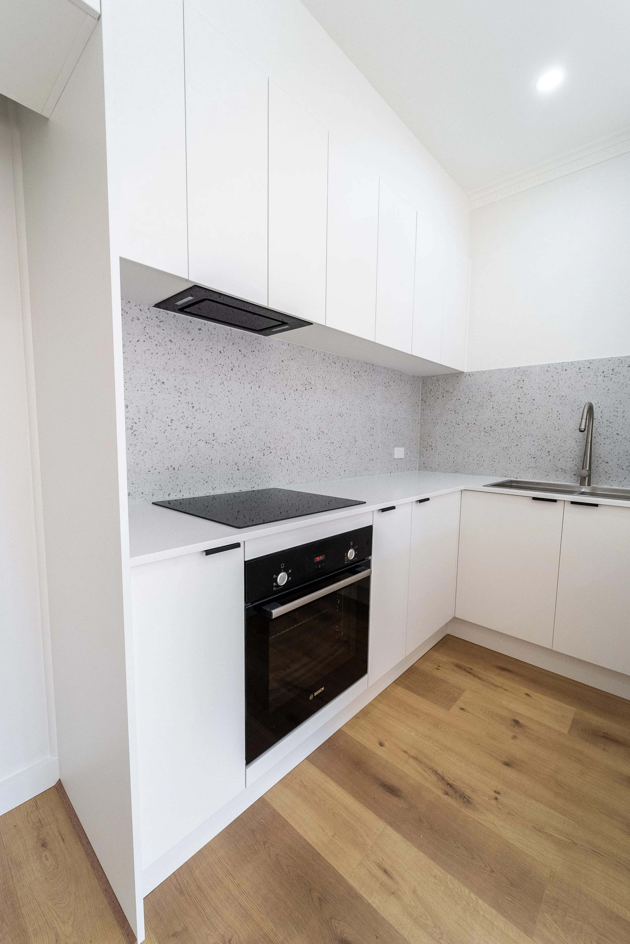 Modern kitchen with white cabinets, speckled gray backsplash, black stove and oven, and a stainless steel sink with a high-arc faucet.