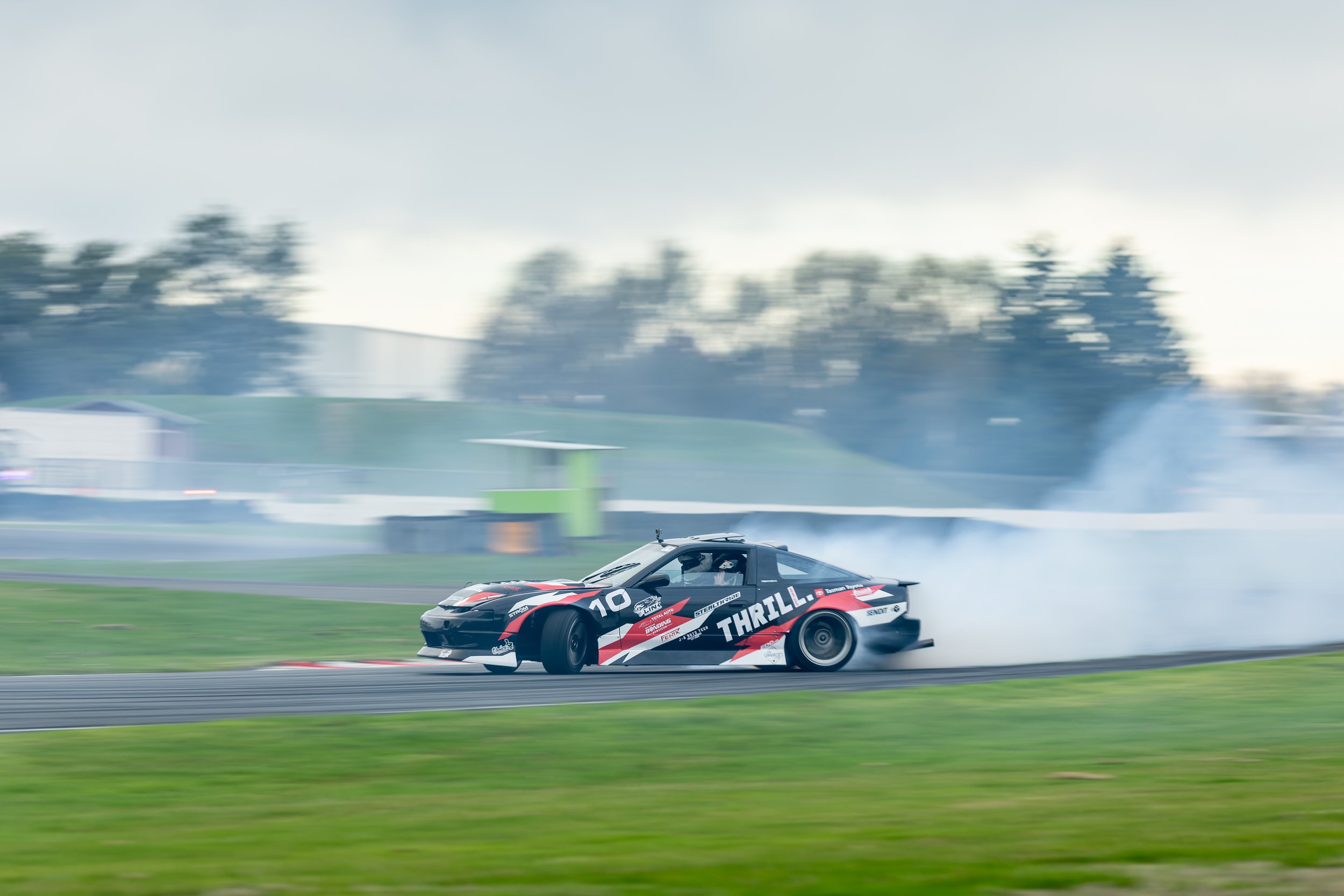 A black race car with red and white graphics skids on a race track, creating smoke as it drifts during a motorsport event.