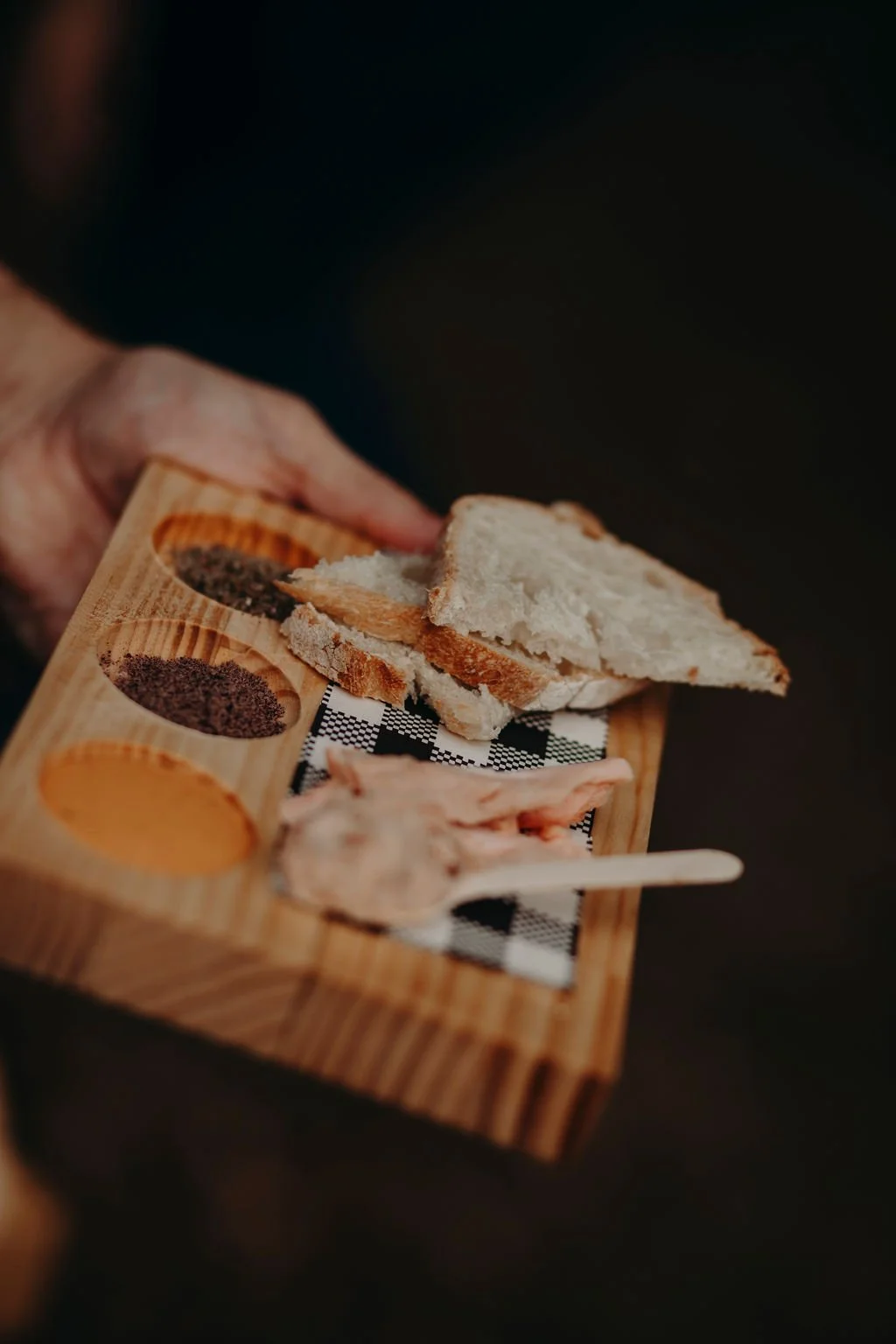 Tasting Trail Tasmania | Close-up of a hand holding a wooden tray with slices of bread and various spices or seasonings and 41º South smoked salmon in small compartments.