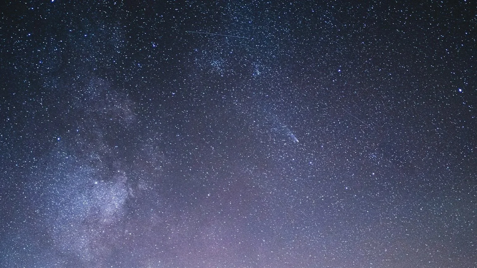 Snow-covered mountain peaks at sunset or sunrise with dark rocky outcroppings.