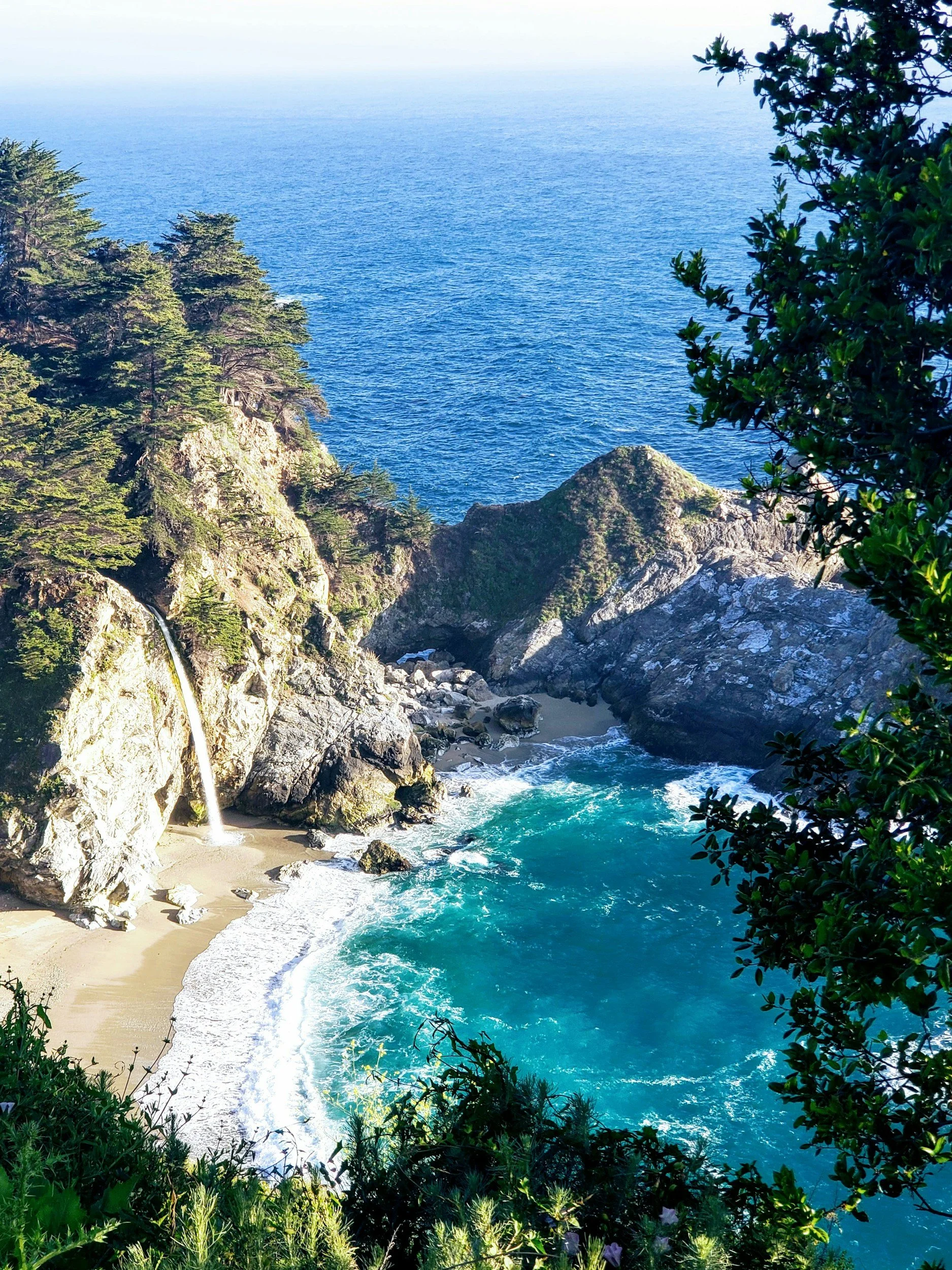 Coastal scene with a small waterfall flowing onto a secluded beach surrounded by cliffs and lush trees, with the ocean extending to the horizon. Online therapy in California, telehealth, LQBTQ+