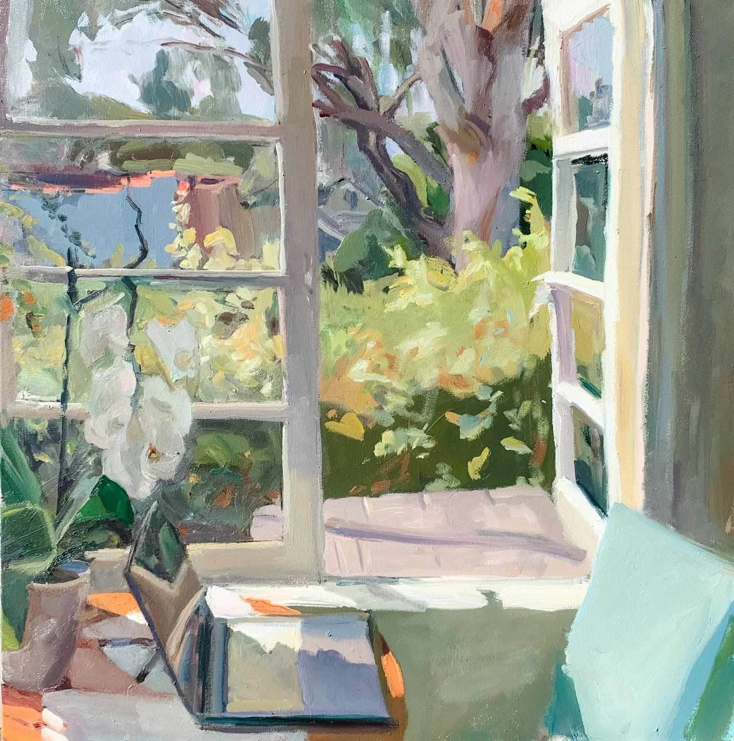 Interior view of a room with an open window looking out to a garden with a large tree and lush greenery. A table with an open macbook and a potted orchid is in the foreground, with sunlight streaming through the window.