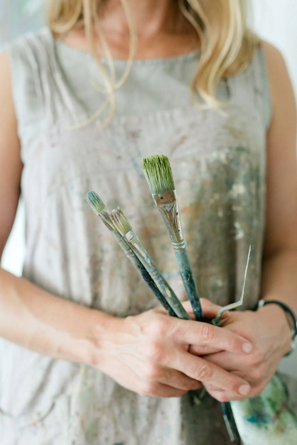 Person holding multiple paintbrushes with paint on them.