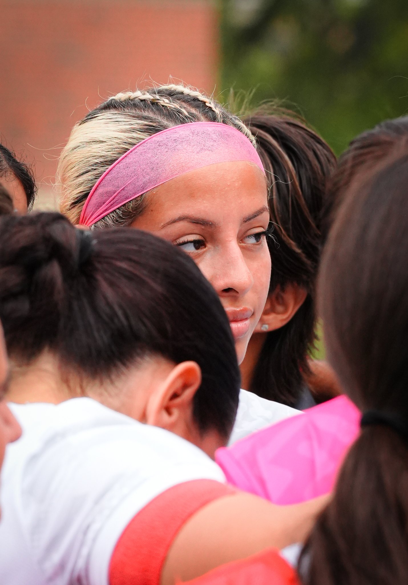 A young girl with blonde and dark hair wearing a pink headband surrounded by other people.