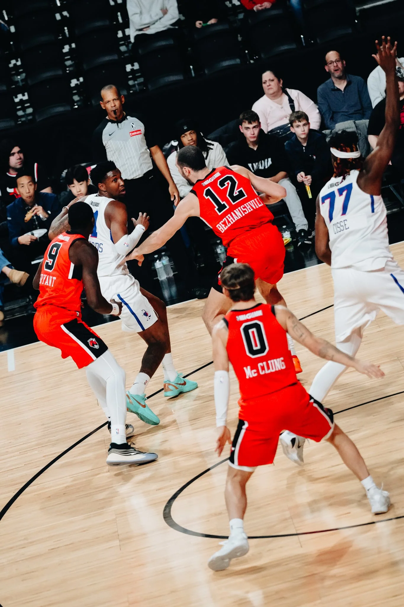 Basketball players in action during a game, with spectators watching from the sidelines.