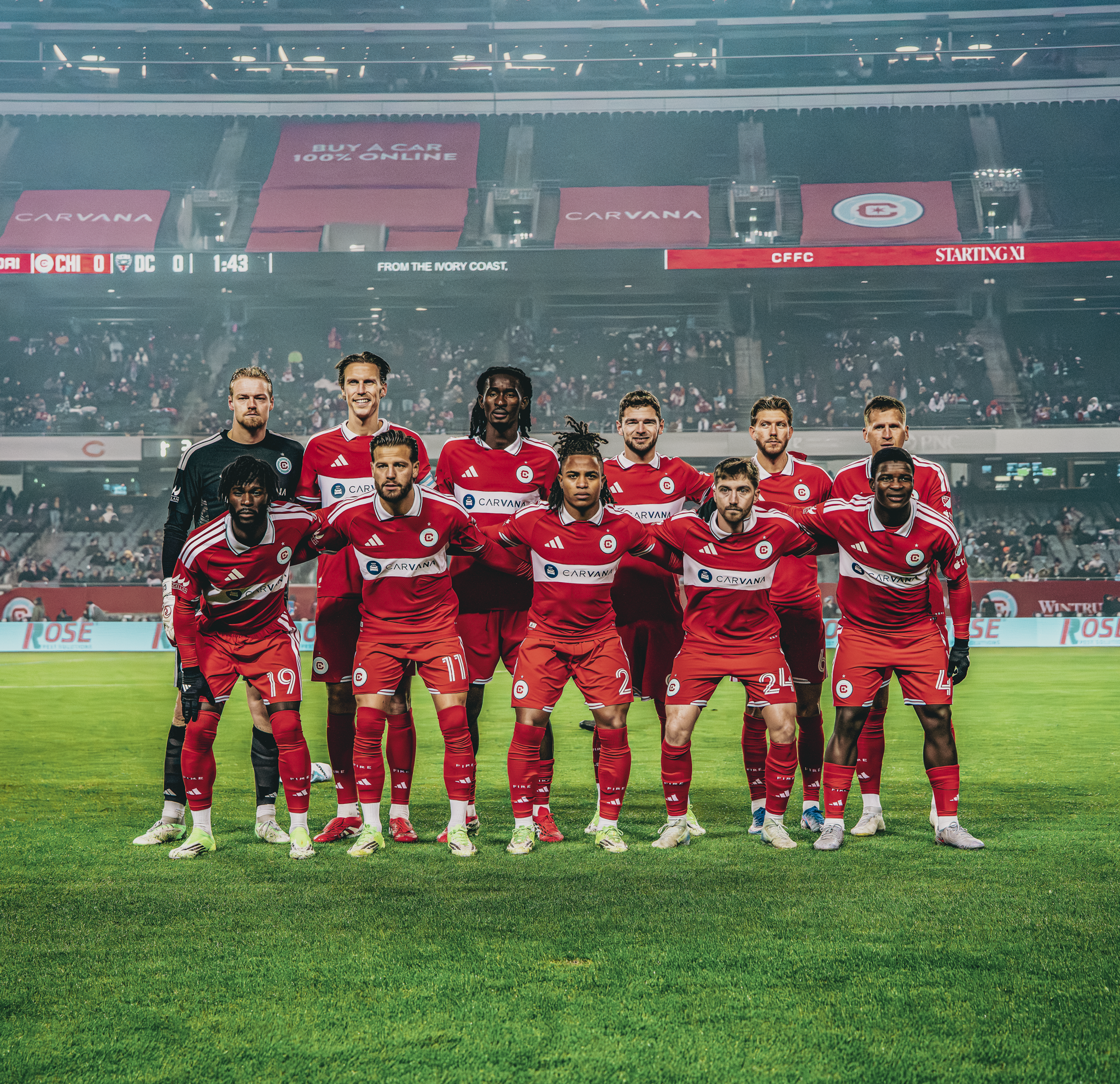 A soccer team in red uniforms posing on the field before a match in a stadium.