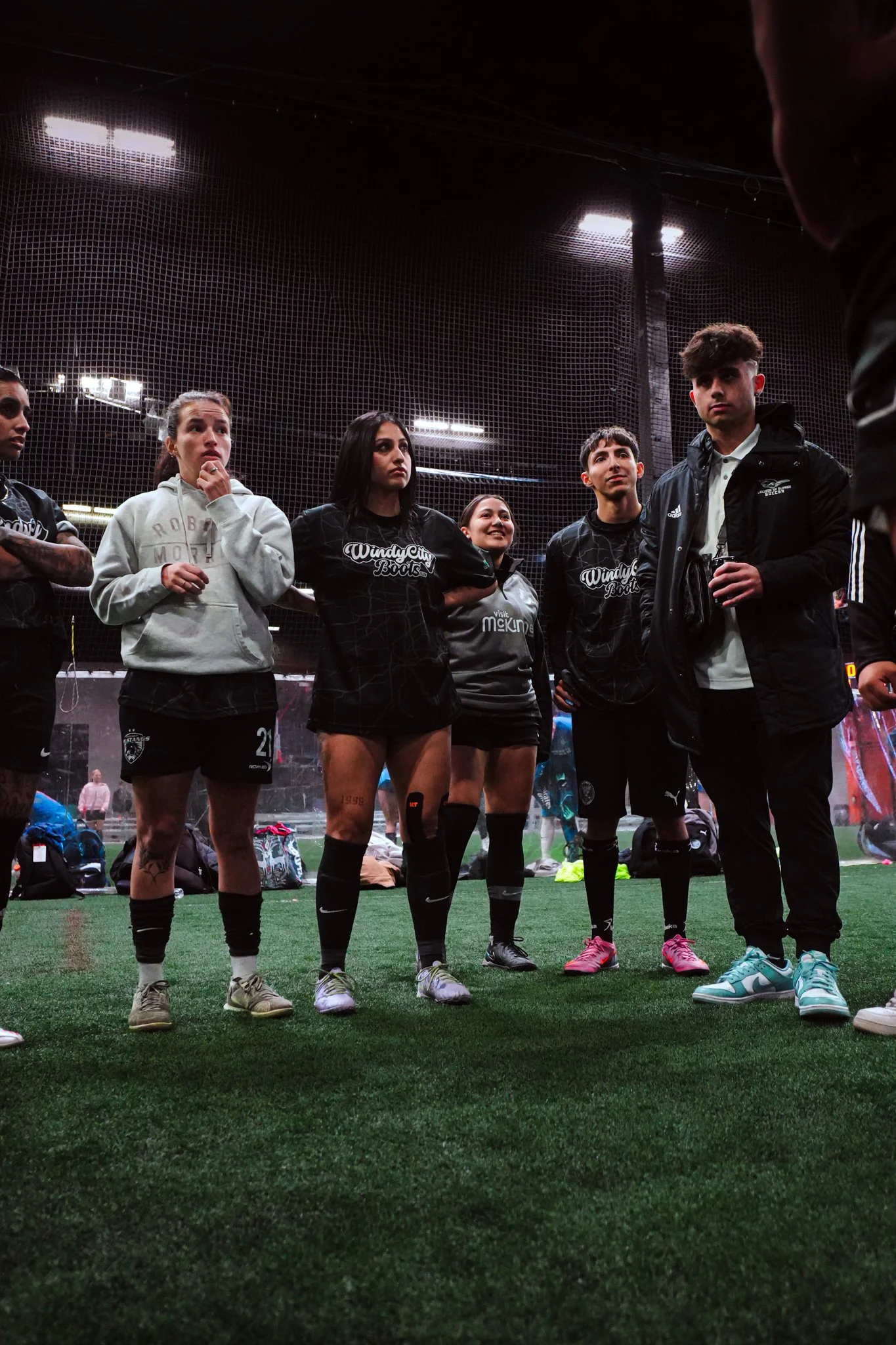 Group of female soccer players and a male coach in an indoor sports facility, listening attentively.