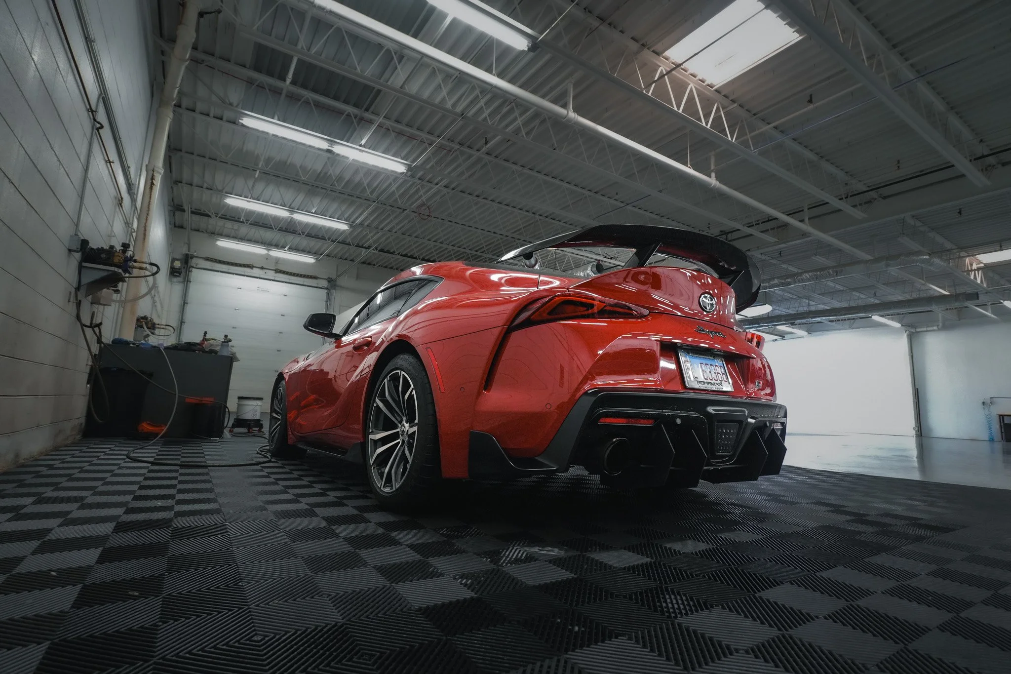 Red sports car with a large rear spoiler inside a garage or workshop.