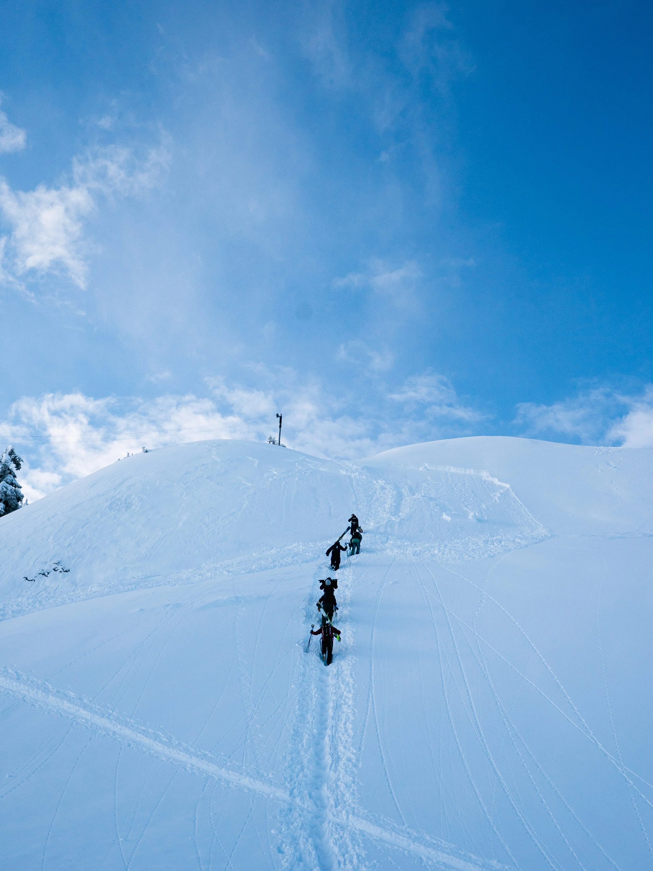 Group of four people hiking up a snow-covered mountain under a blue sky with some clouds.