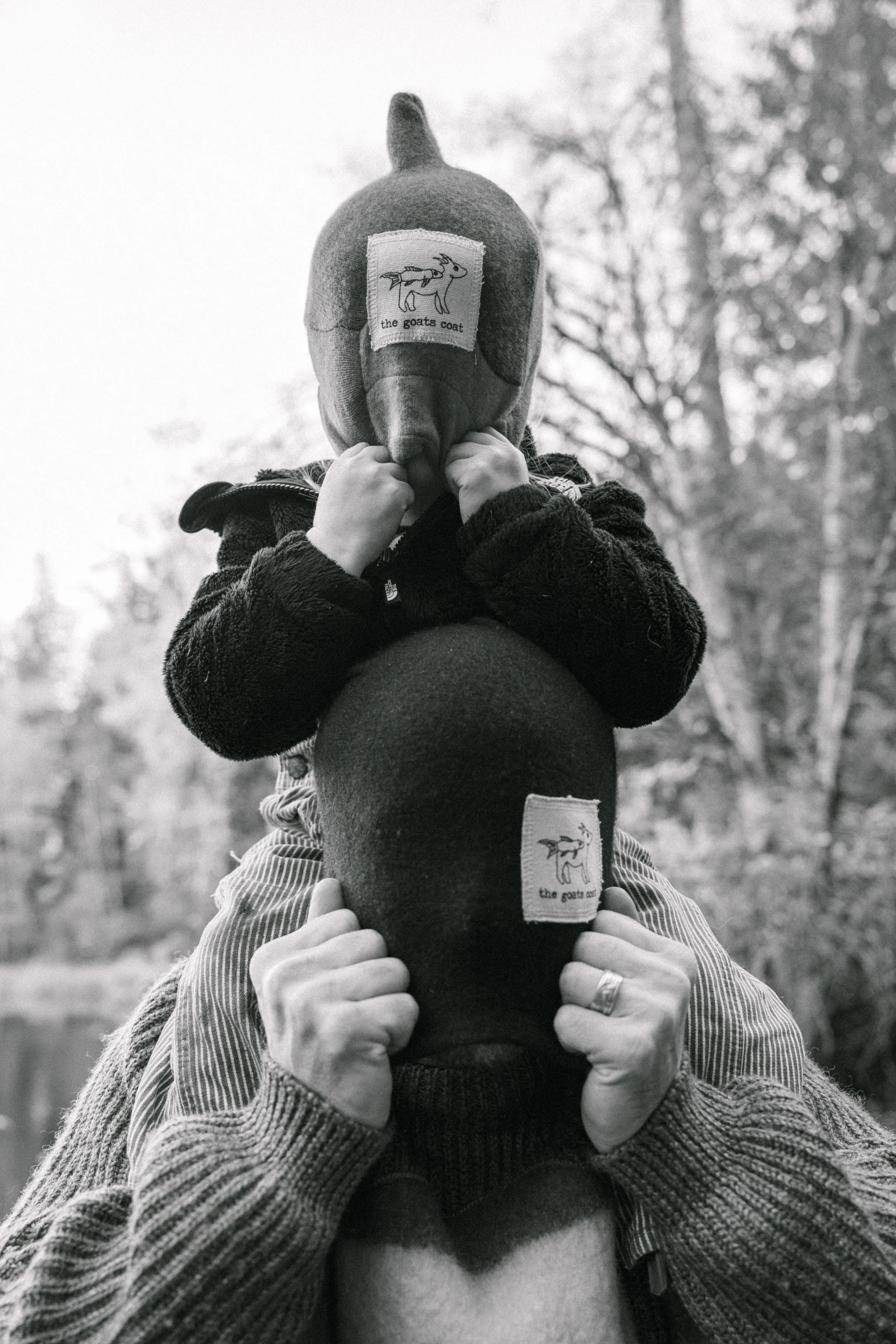 Son sits on father's shoulders while both pull beanies over their eyes.
