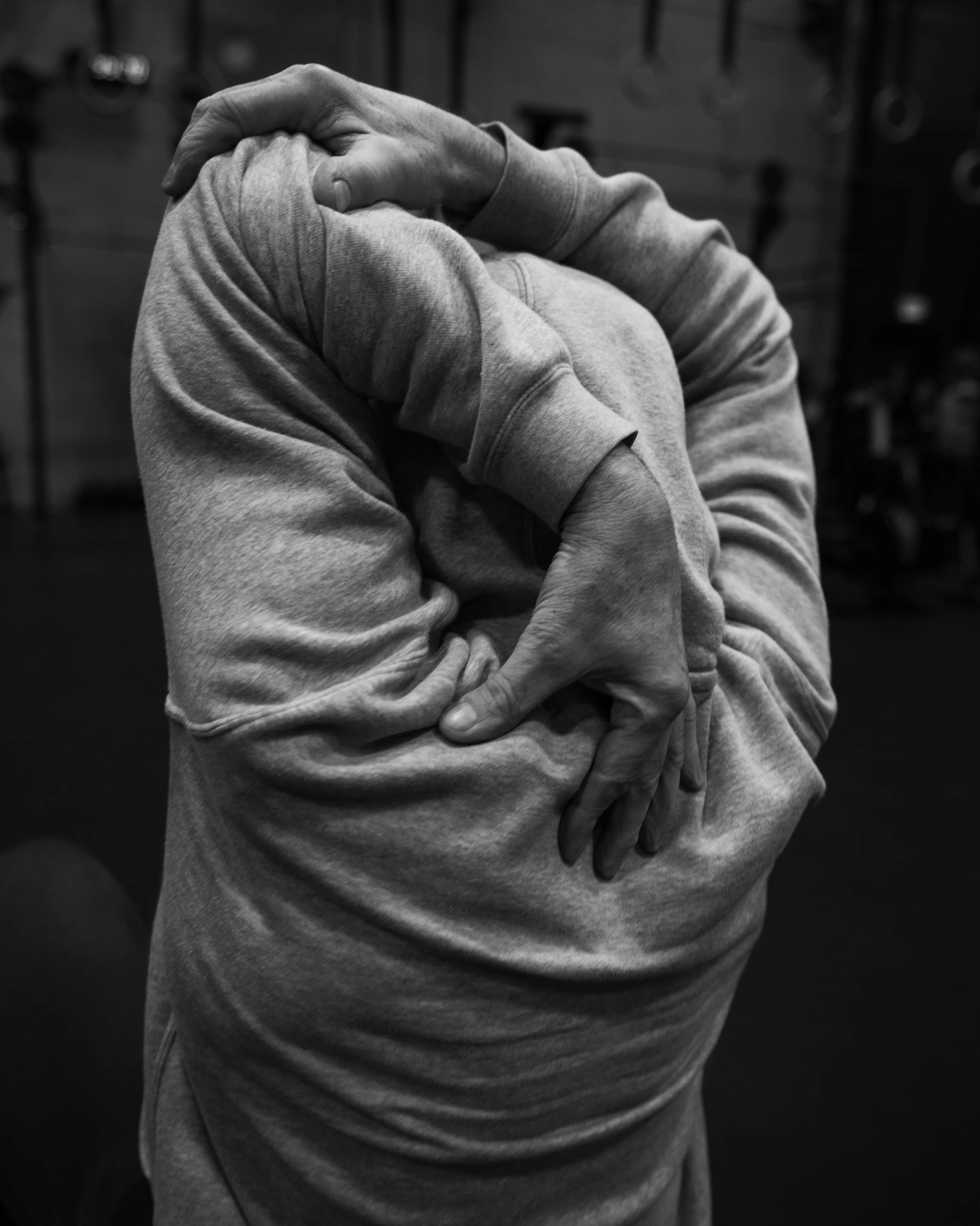 A person stretching their arm across their chest in a gym, wearing a hoodie.