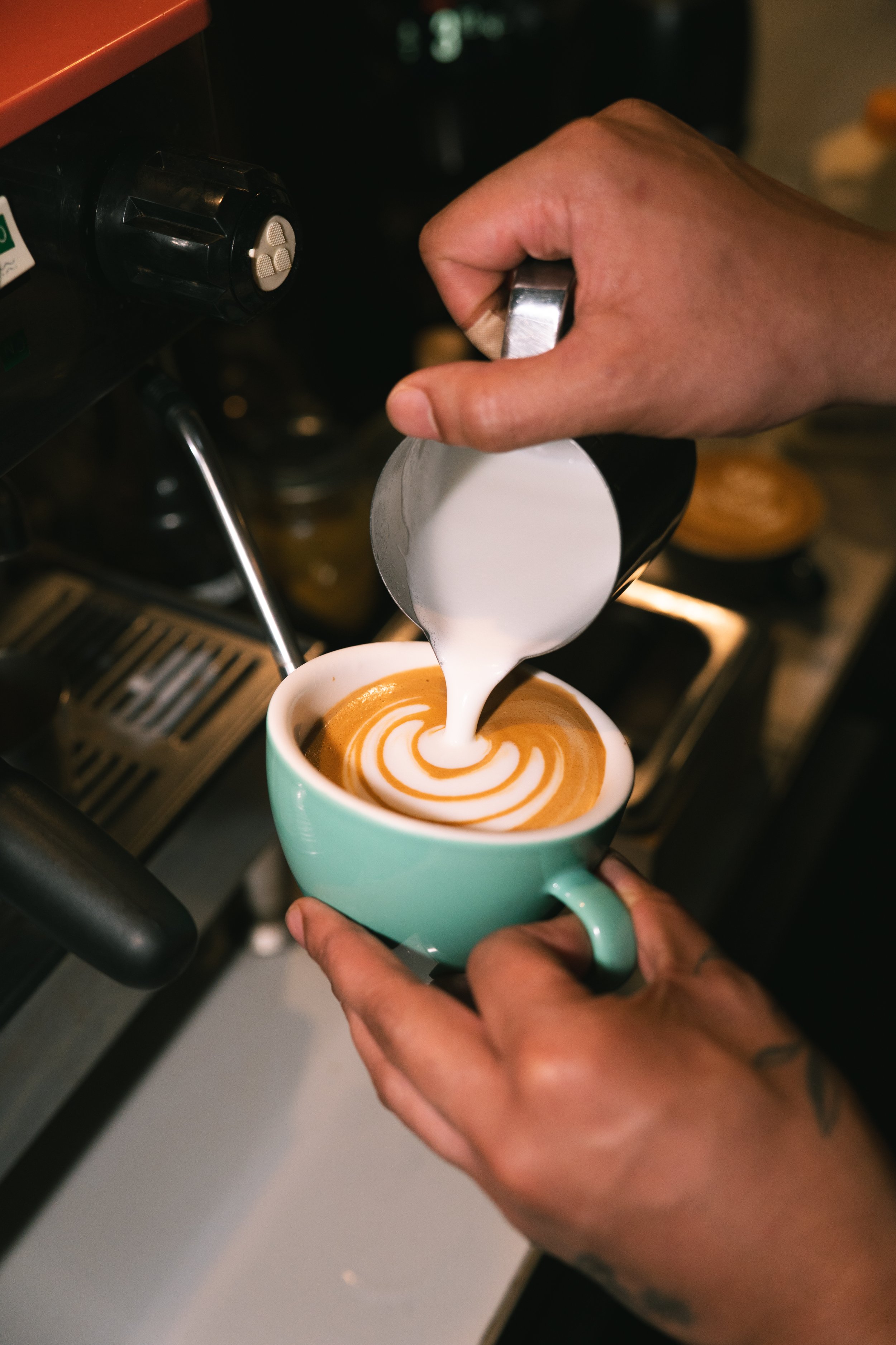 Barista pouring milk into a cup of espresso to create latte art.