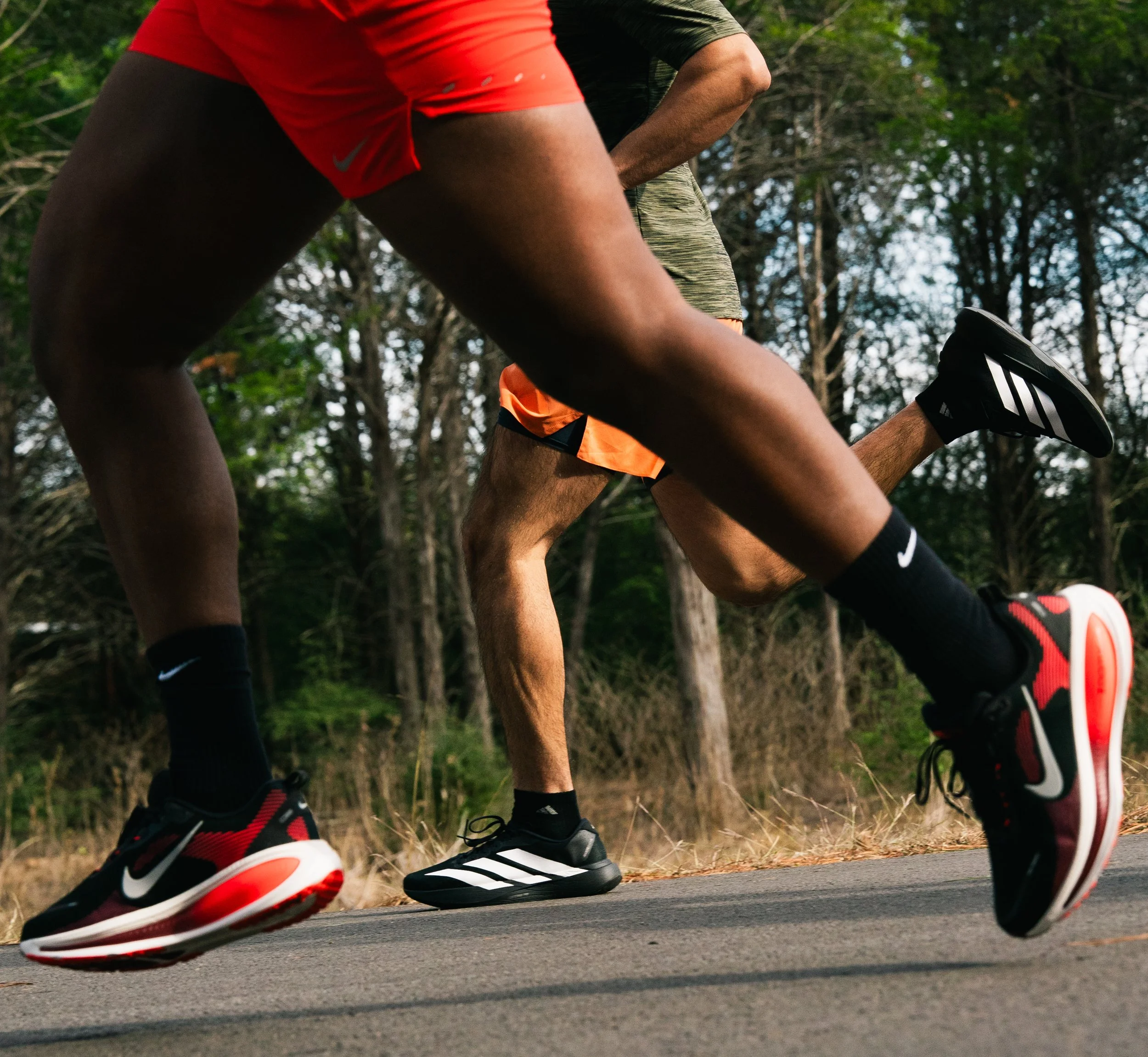 Close-up of two runners' legs in motion during a race on a paved road surrounded by trees.