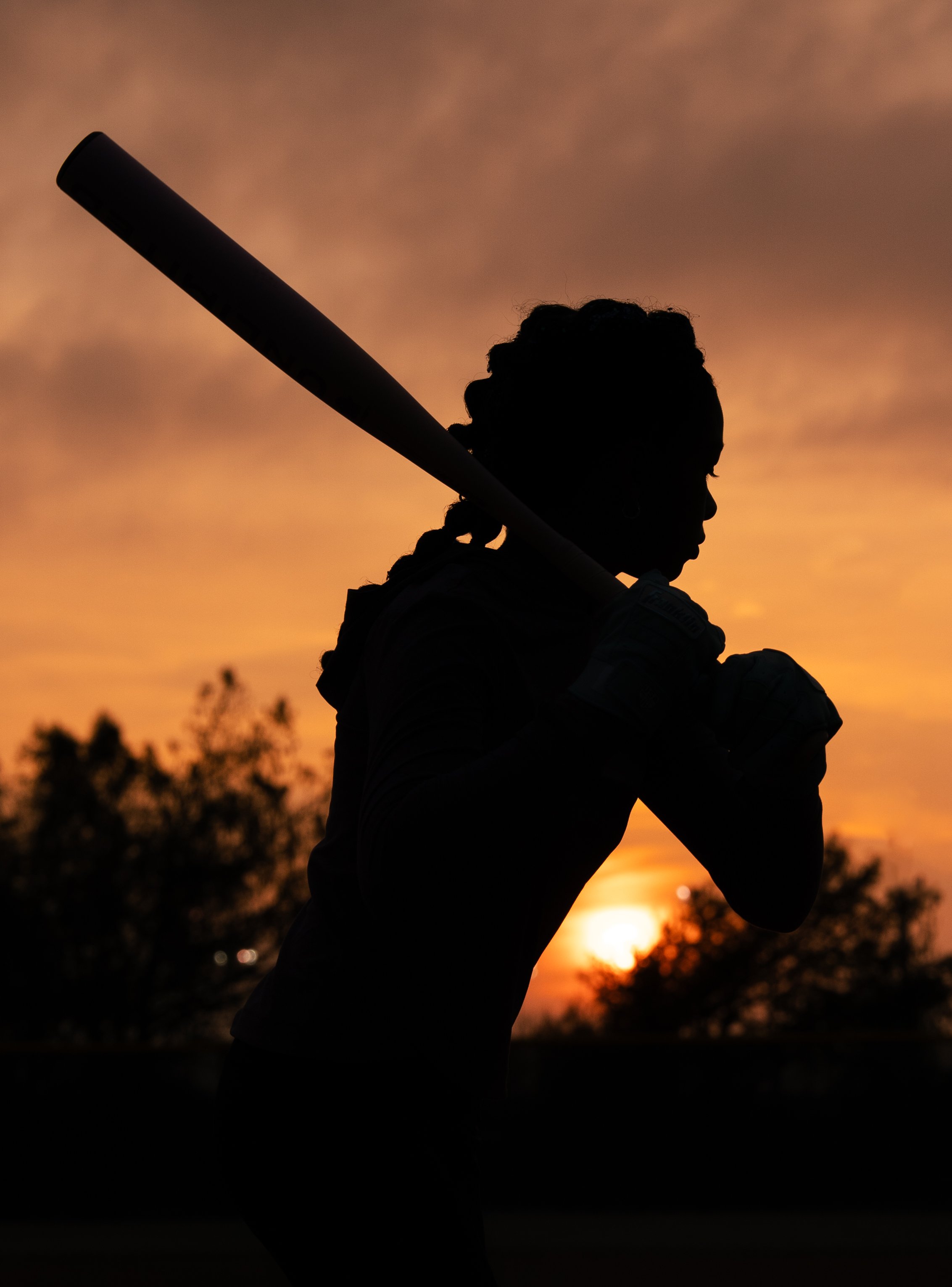 Silhouette of a woman holding a baseball bat on a sunset background.