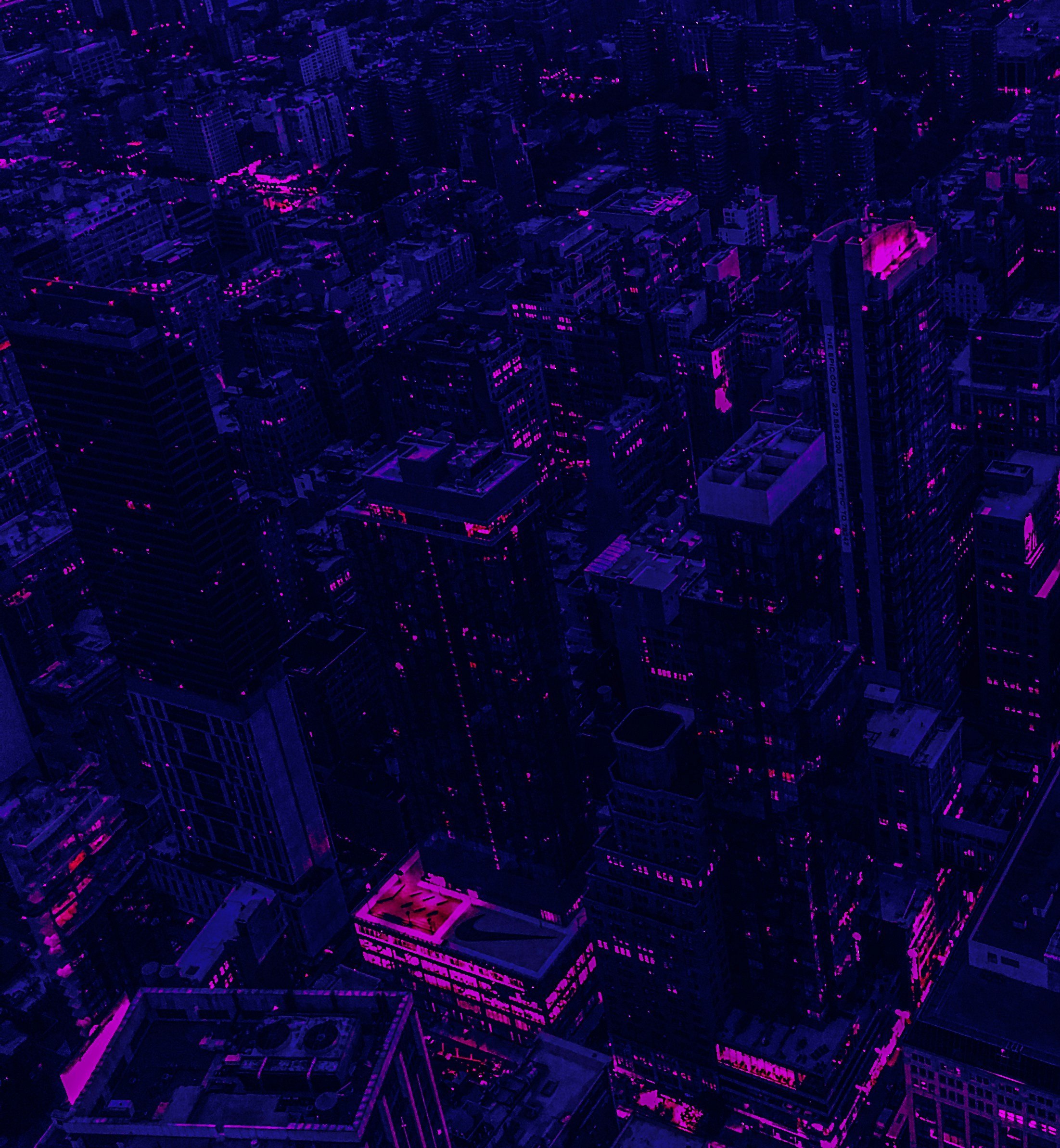 Night view of a city skyline with tall buildings illuminated by pink and purple lights.