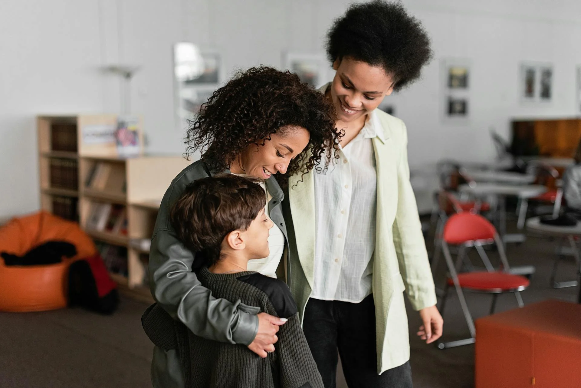 Three people, two women and a young boy, smiling and hugging in a classroom setting.