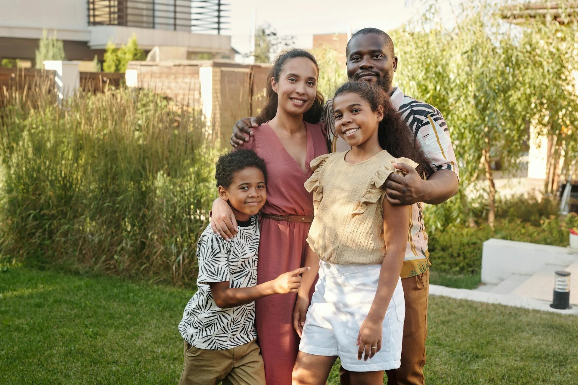 A happy multigenerational family of five standing outdoors in a garden, smiling and embracing each other during daytime.