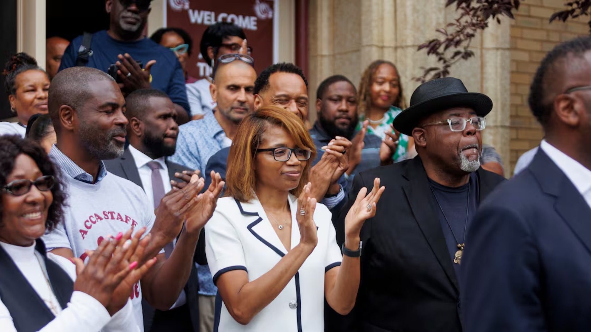A diverse group of people standing outdoors, clapping and paying tribute during a ceremony or event.
