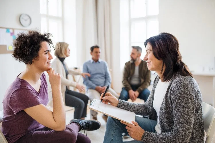 Therapist taking notes during a counseling session with young woman in a group therapy setting