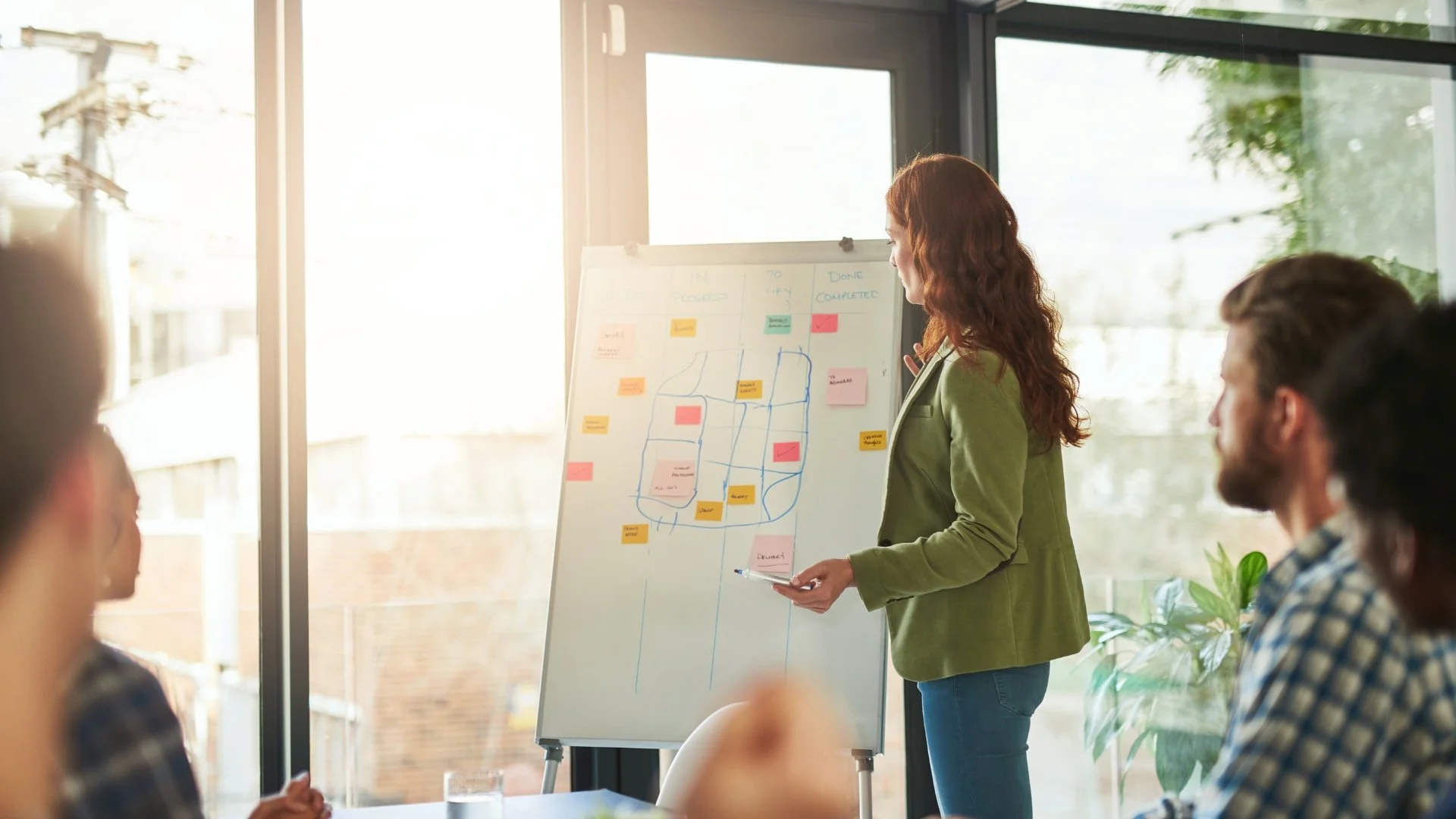 A woman presenting a sports strategy diagram on a whiteboard to a group of people in a bright, modern conference room.