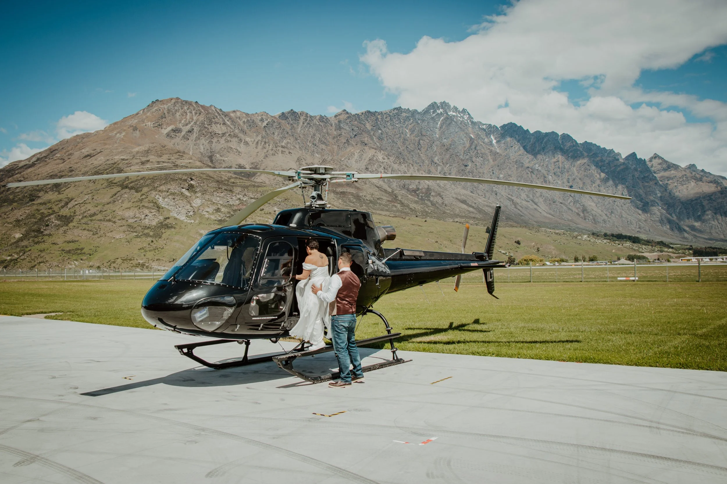 Couple getting into a helicopter on the runway with alpine mountains behind them for heli elopement