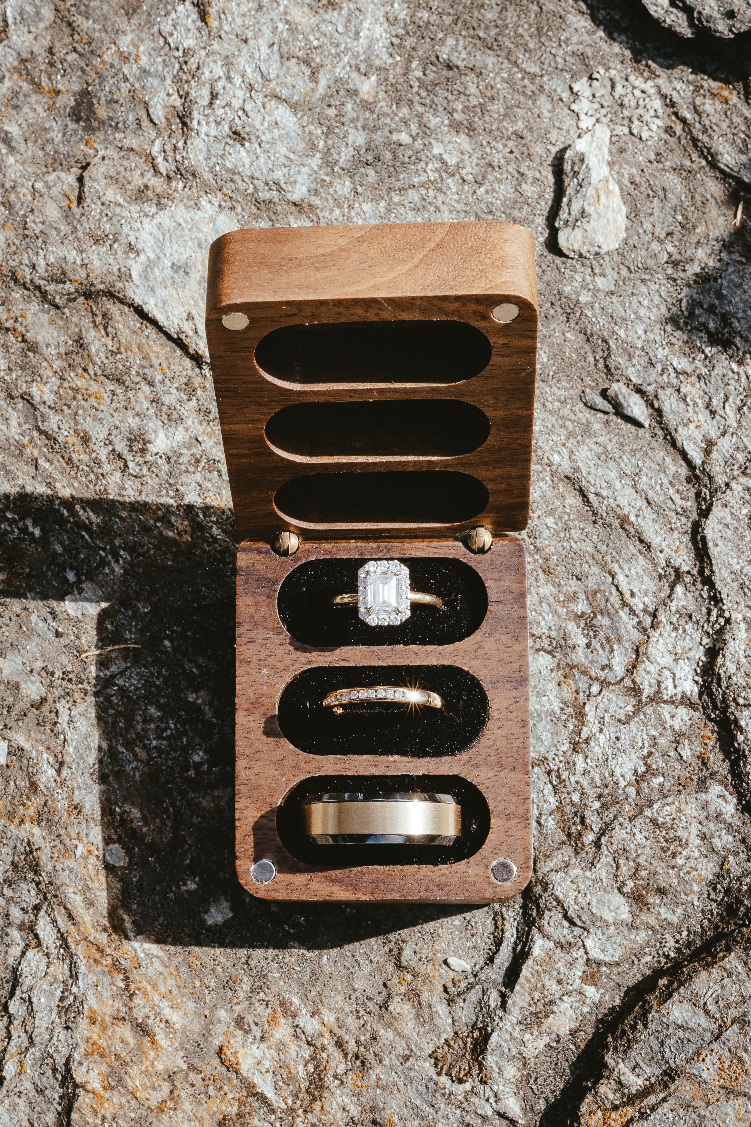 An open wooden box displaying five rings on a rocky surface.