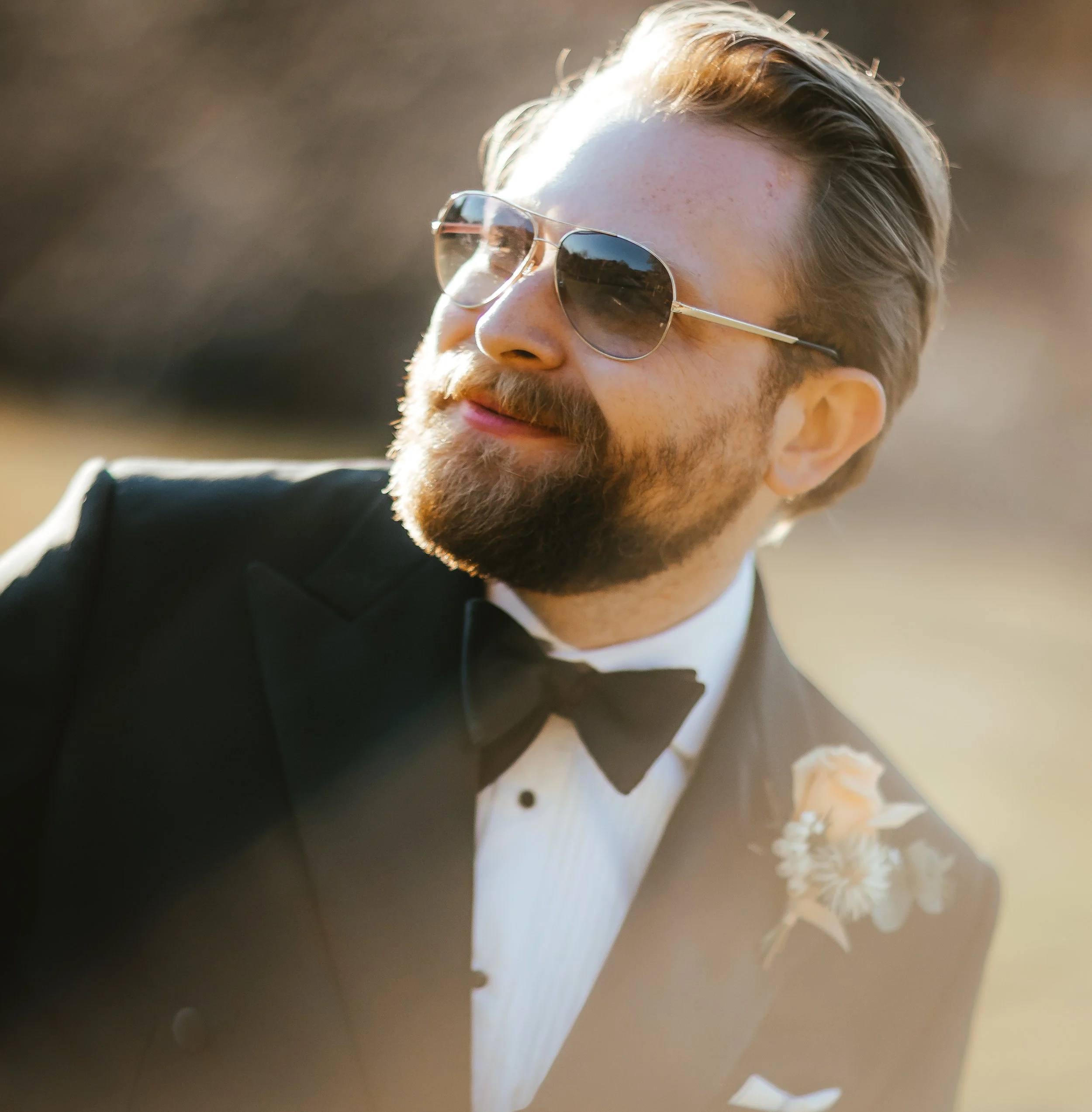 Close-up of a person's face wearing sunglasses, with light-colored hair and facial hair, outdoors in natural light.