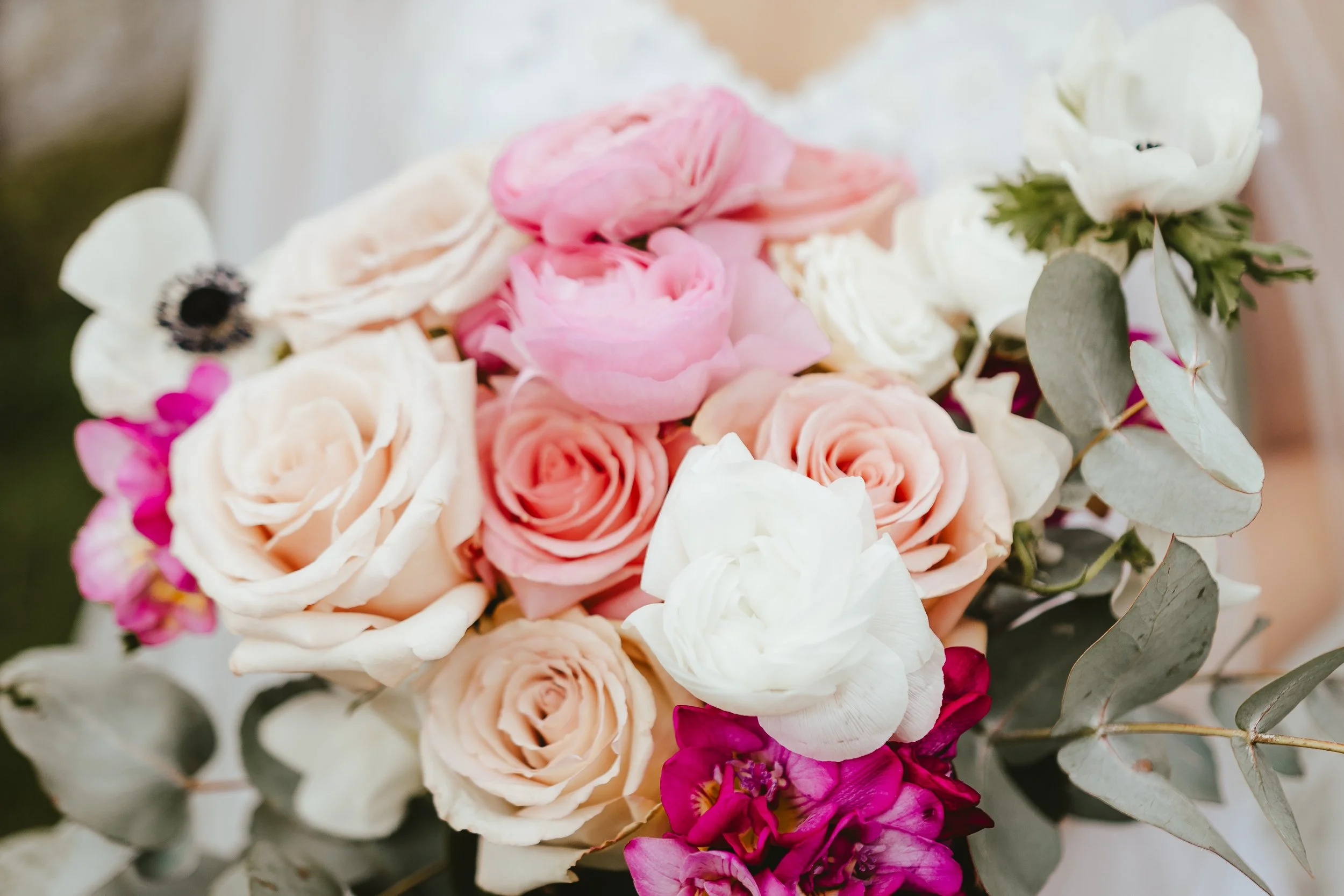 A close-up of a bouquet of flowers including pink roses, white anemones, and pink and purple stock flowers, with greenery.