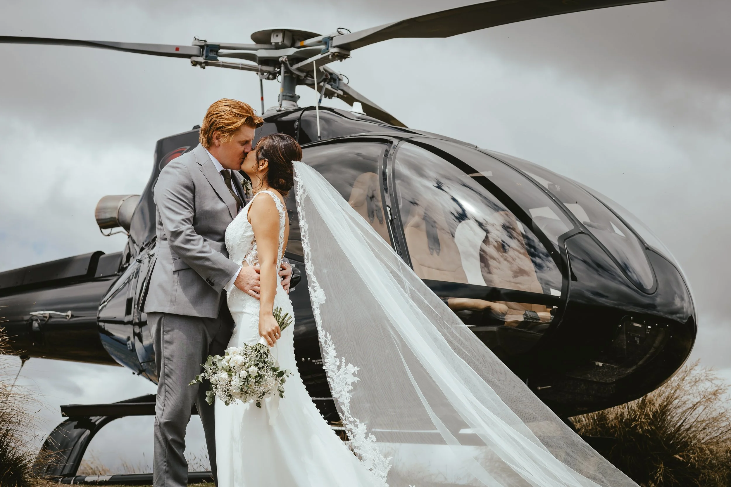 Bride and groom kissing in front of a helicopter at Coromandel Peak during their unforgettable heli elopement.