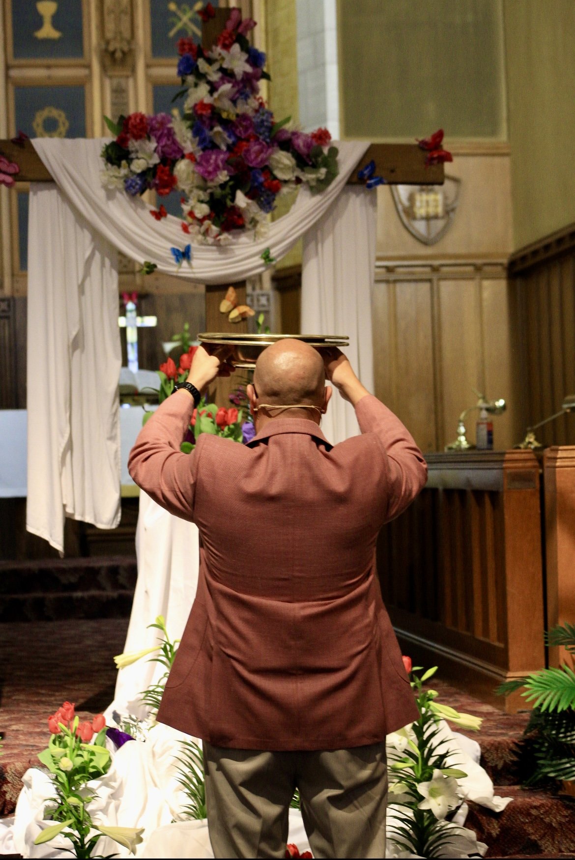 A man in a brown suit adjusting a golden tray on his head inside a decorated church.