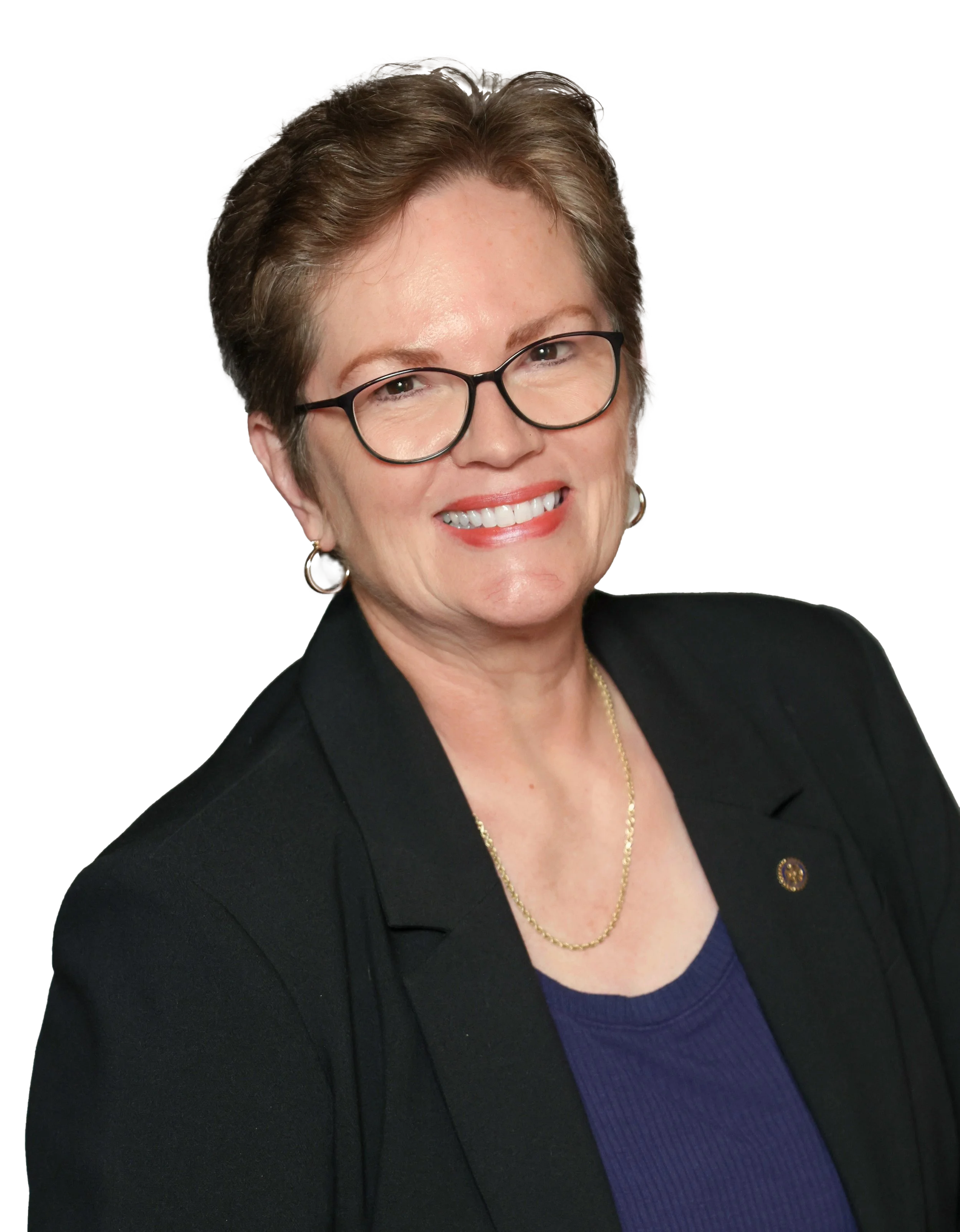 A woman with short brown hair, glasses, and earrings, smiling, wearing a black blazer over a blue top with a gold necklace.