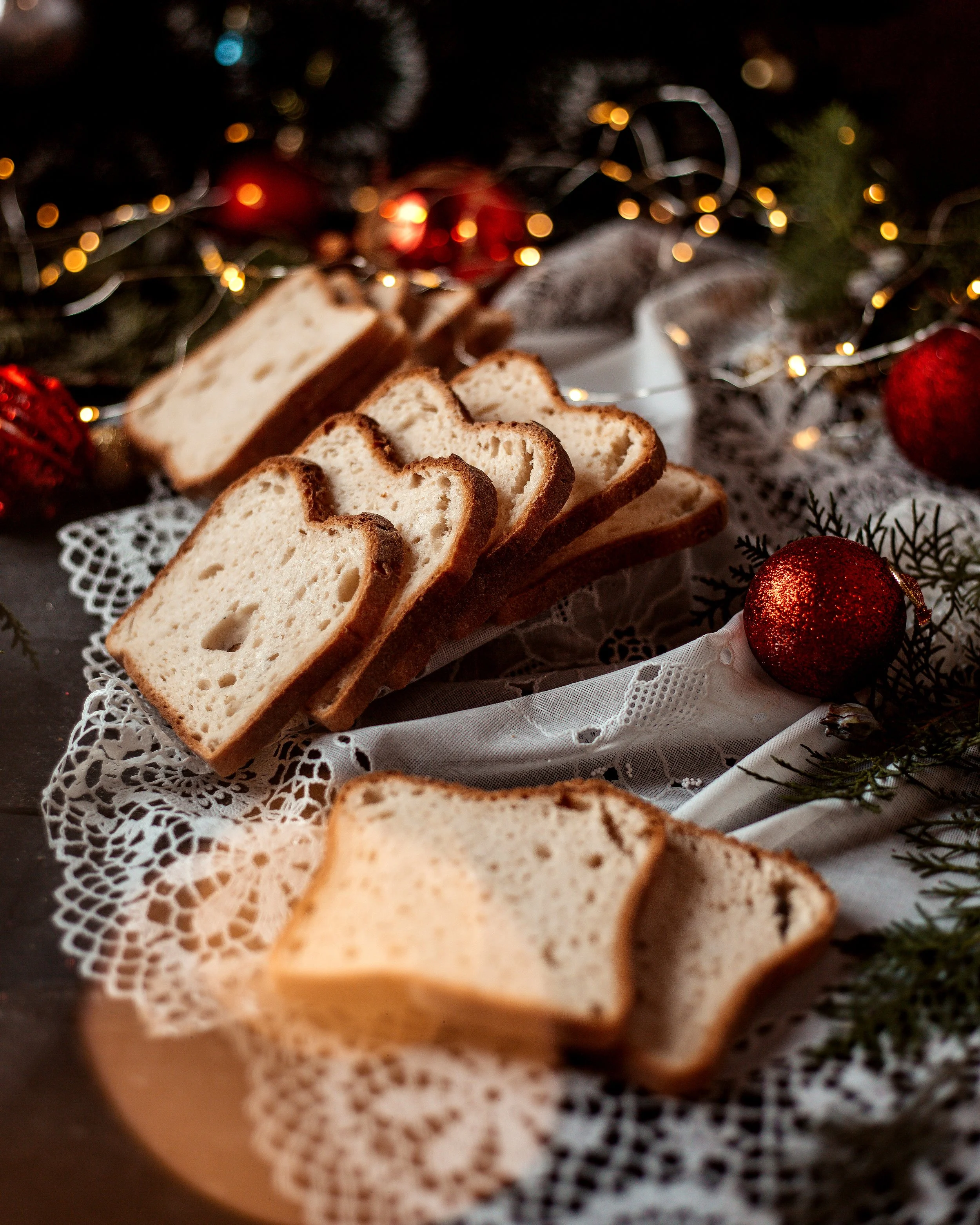 Slices of bread arranged on a white lace cloth with Christmas ornaments and greenery in the background.