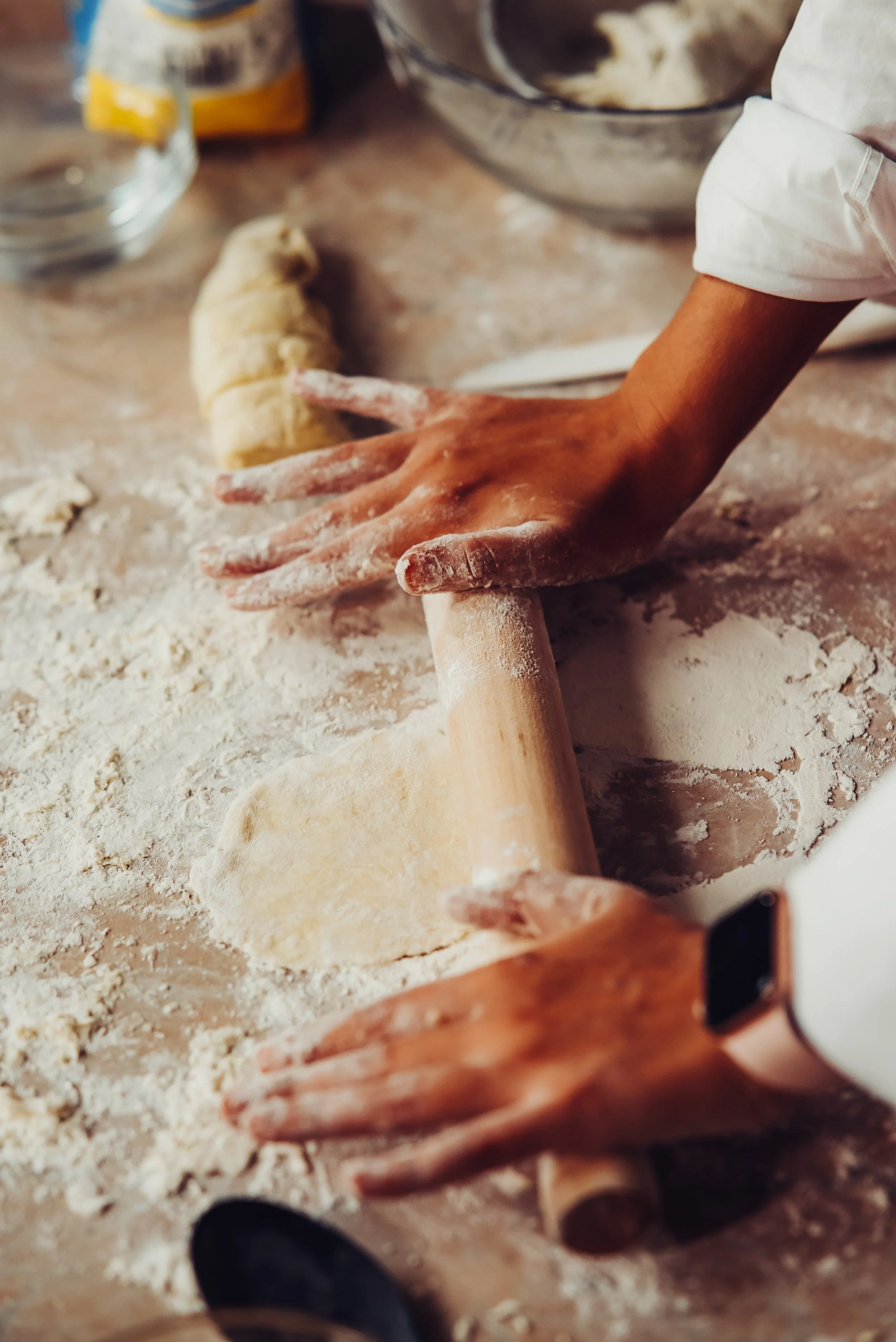 Hands rolling out dough on a floured surface with a rolling pin